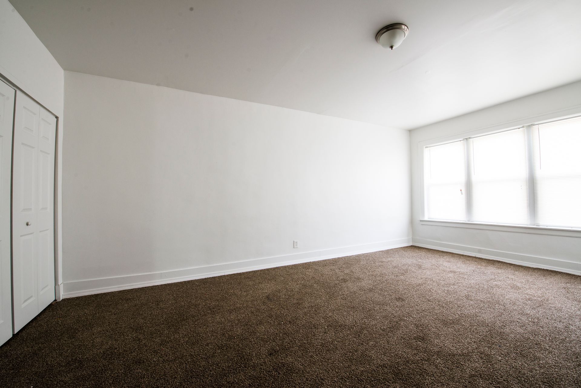 Empty room with white walls, brown carpet, and a window.