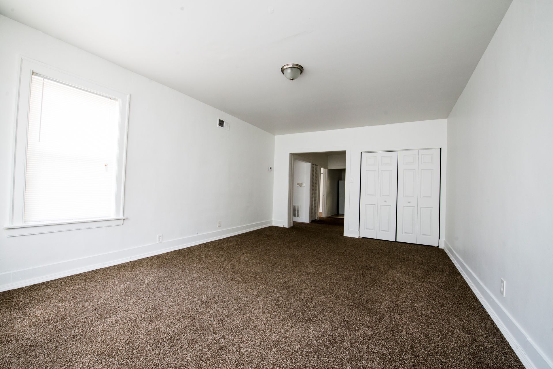 Empty room with brown carpet, white walls, closet, and a window.