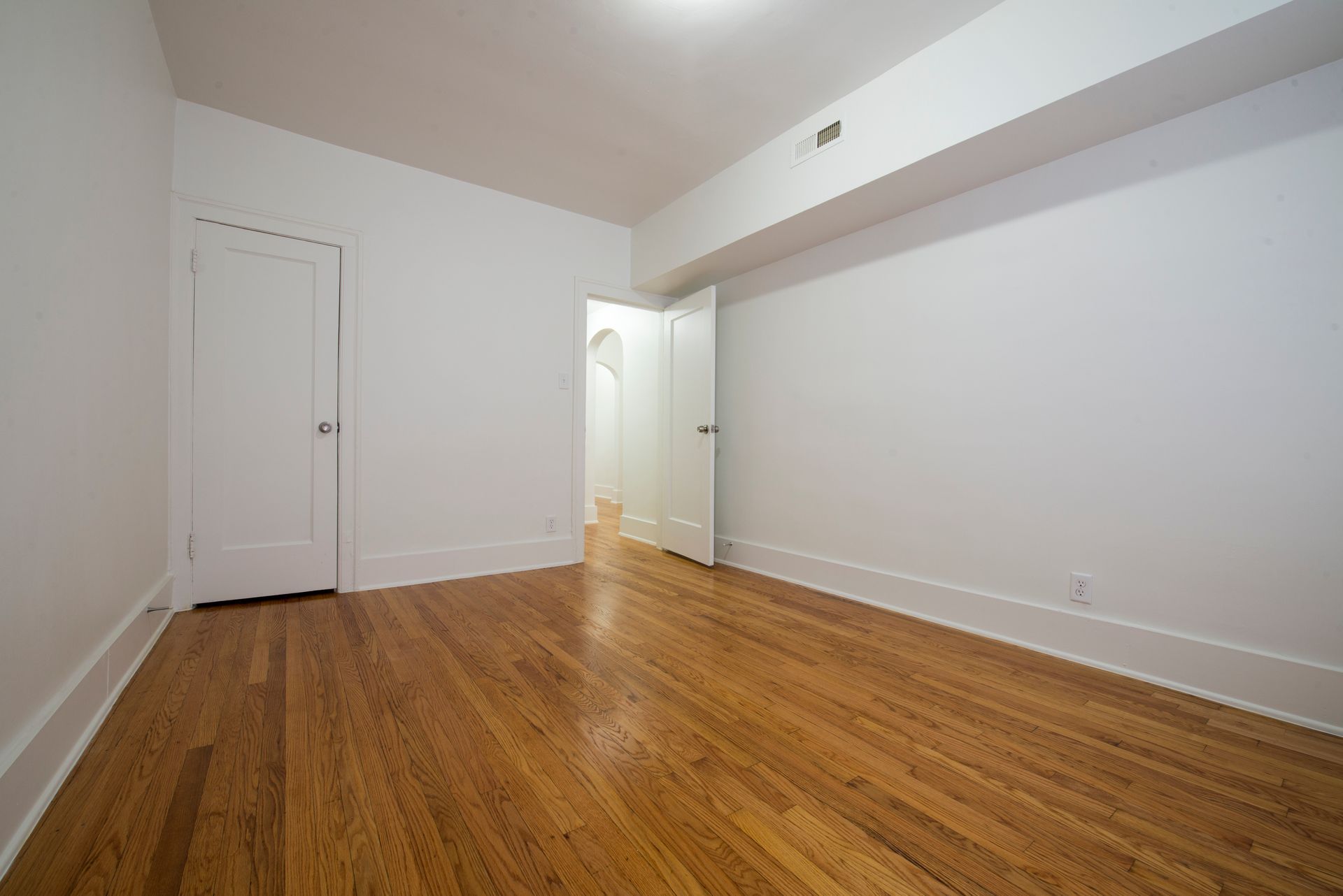 Empty room with hardwood floors, white walls, and two closed doors.