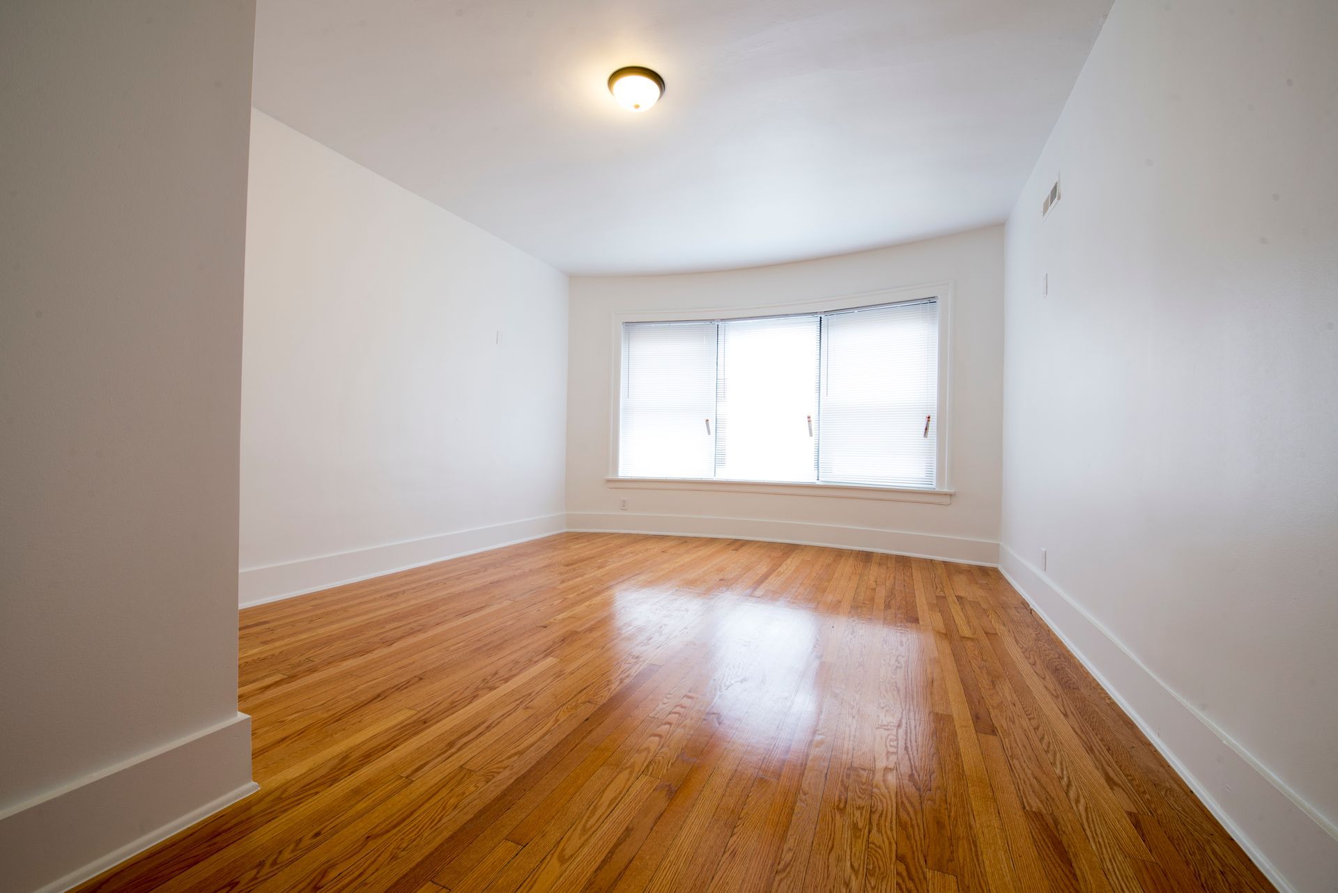 Empty room with hardwood floors, white walls, and a window.