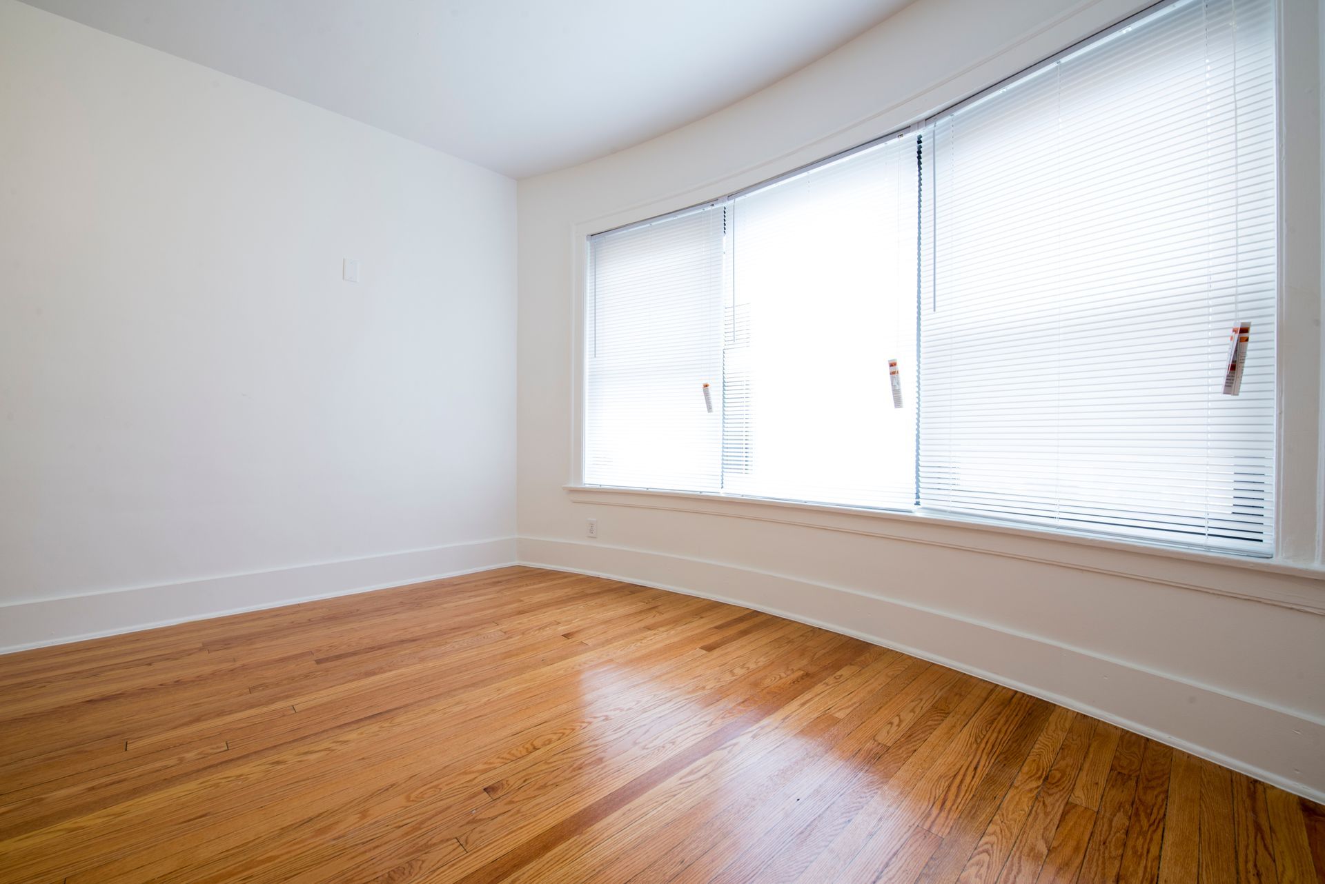 Empty room with wood floor and large window with blinds.