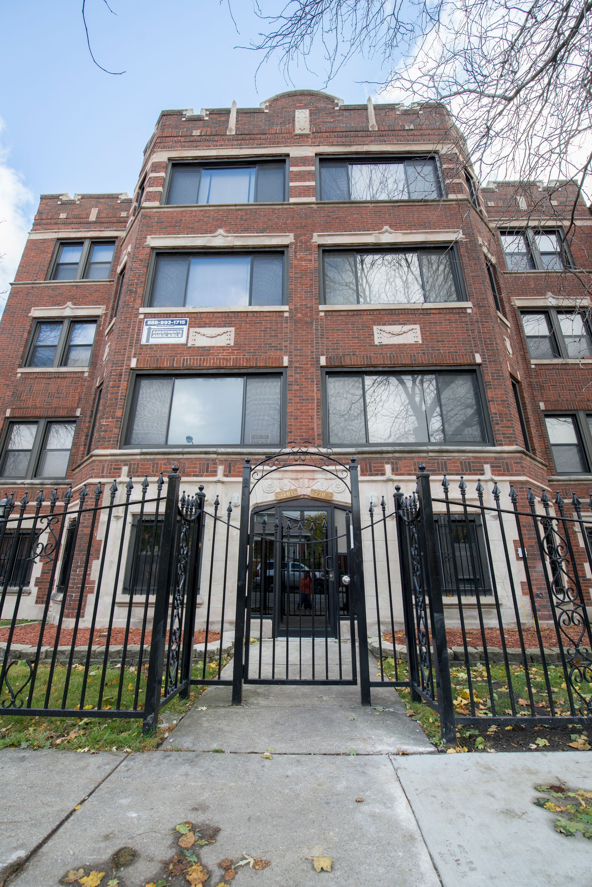 Brick apartment building with black iron gate, blue sky.