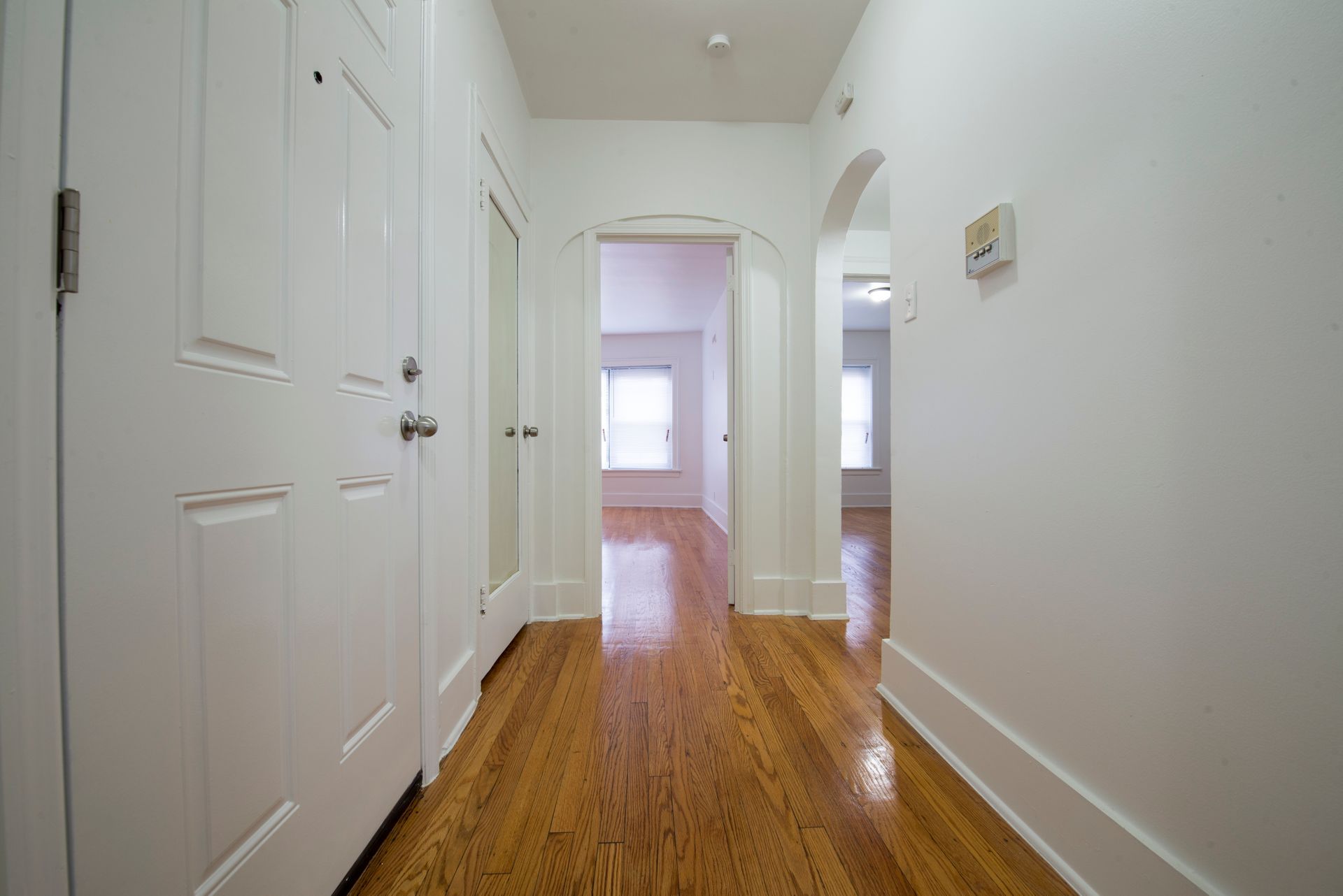 Hallway with white walls, wood floor, and doors leading to rooms.