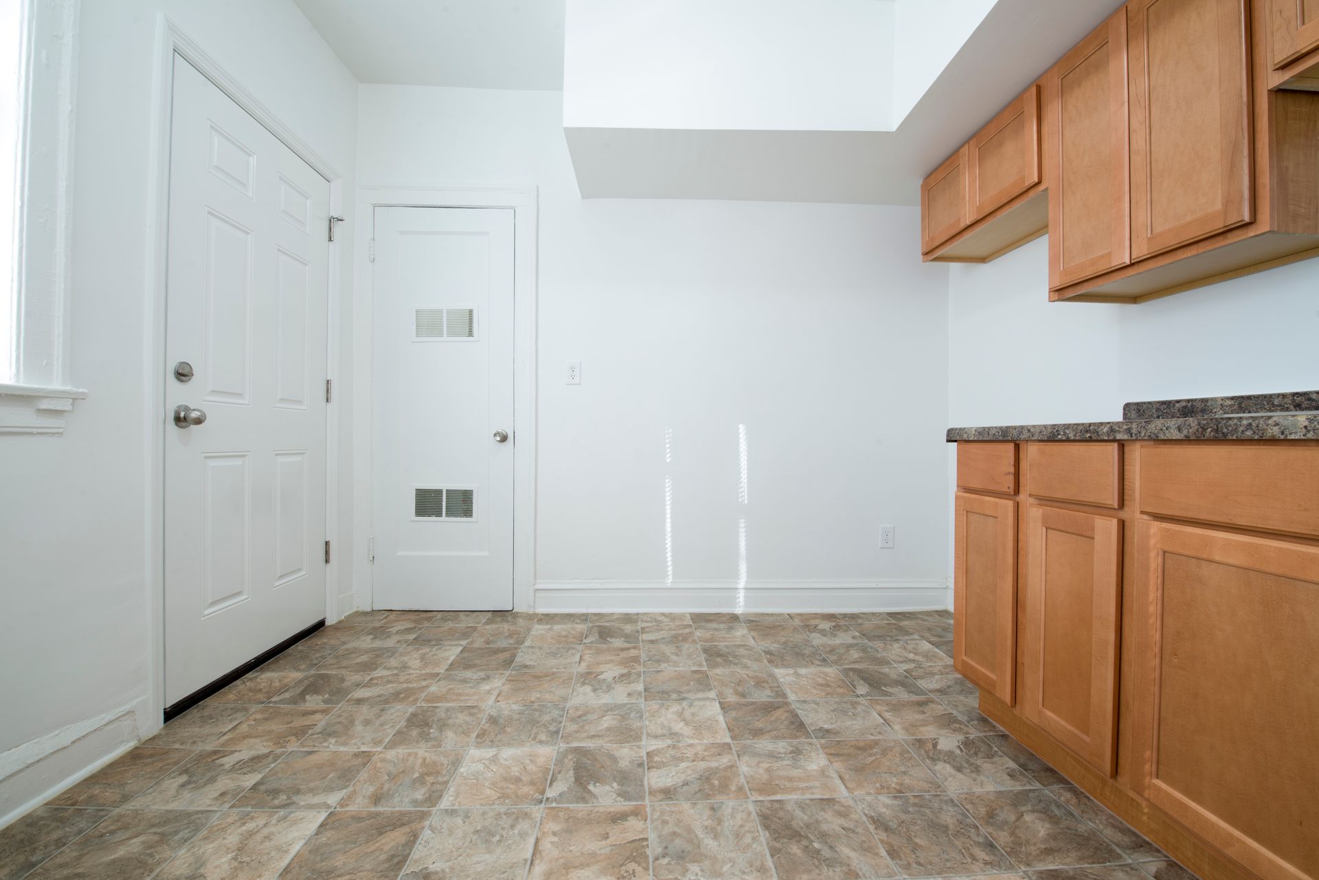 Kitchen with wooden cabinets, a door, and patterned flooring. White walls and a countertop are also visible.
