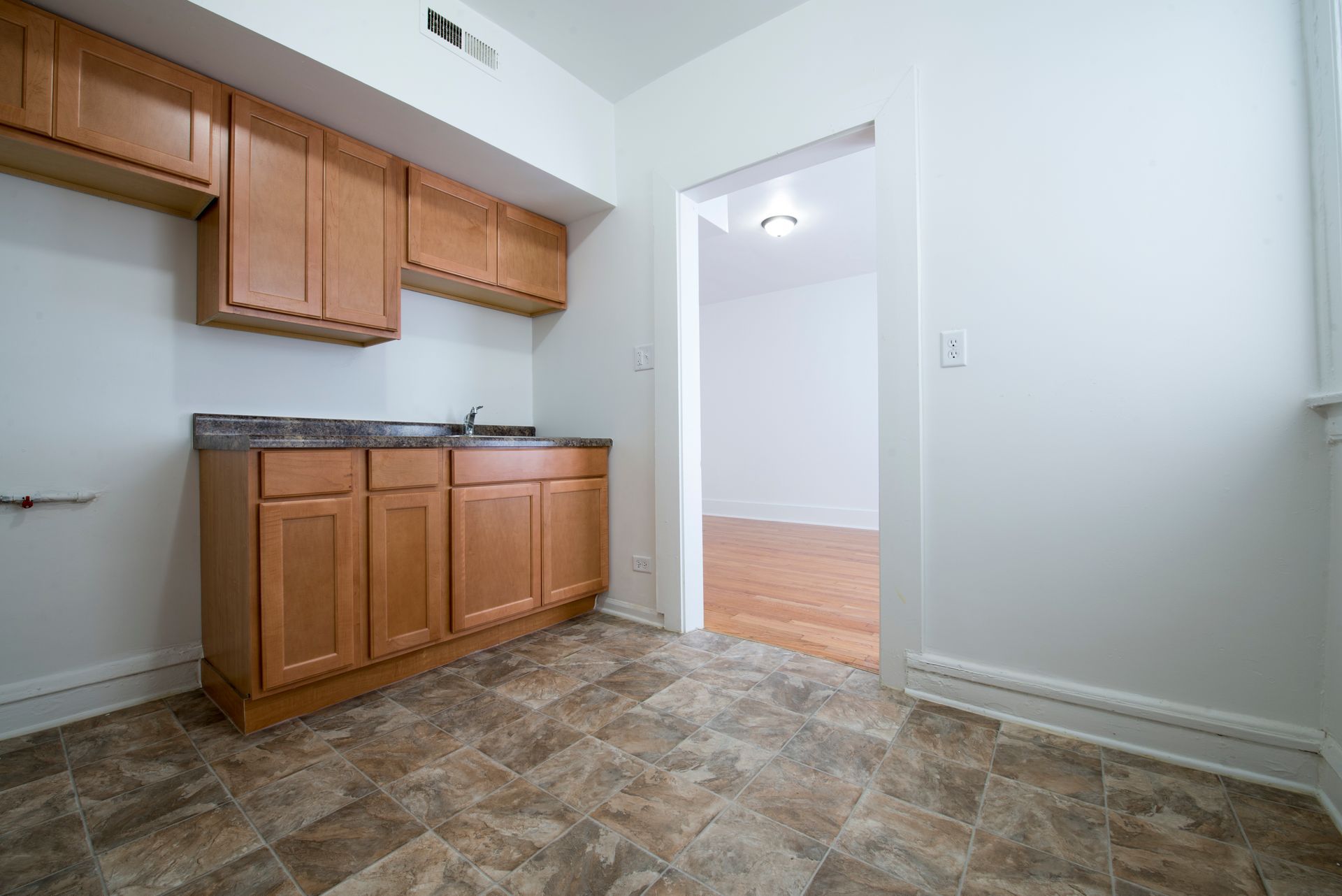 Kitchen with light brown cabinets, dark countertop, and tile floor, with an open doorway to another room.