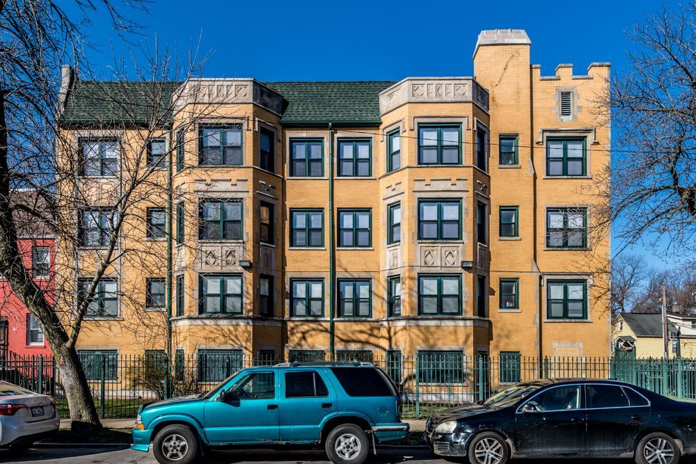 Yellow multi-story apartment building with turquoise SUV and black car parked in front.