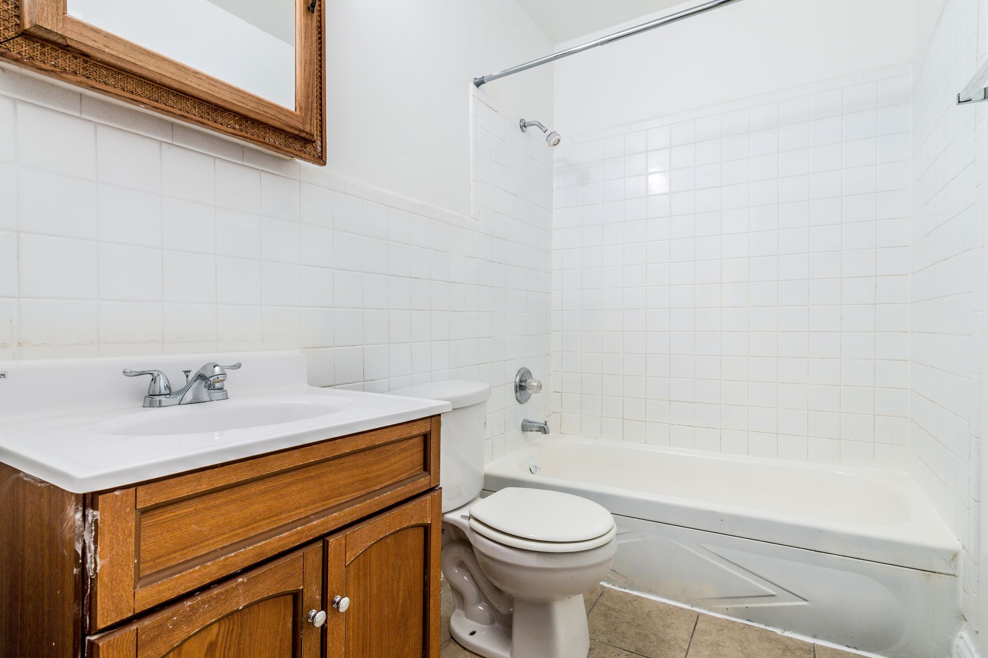 Bathroom with white tile walls, a vanity with wooden cabinets, and a bathtub/shower combo.