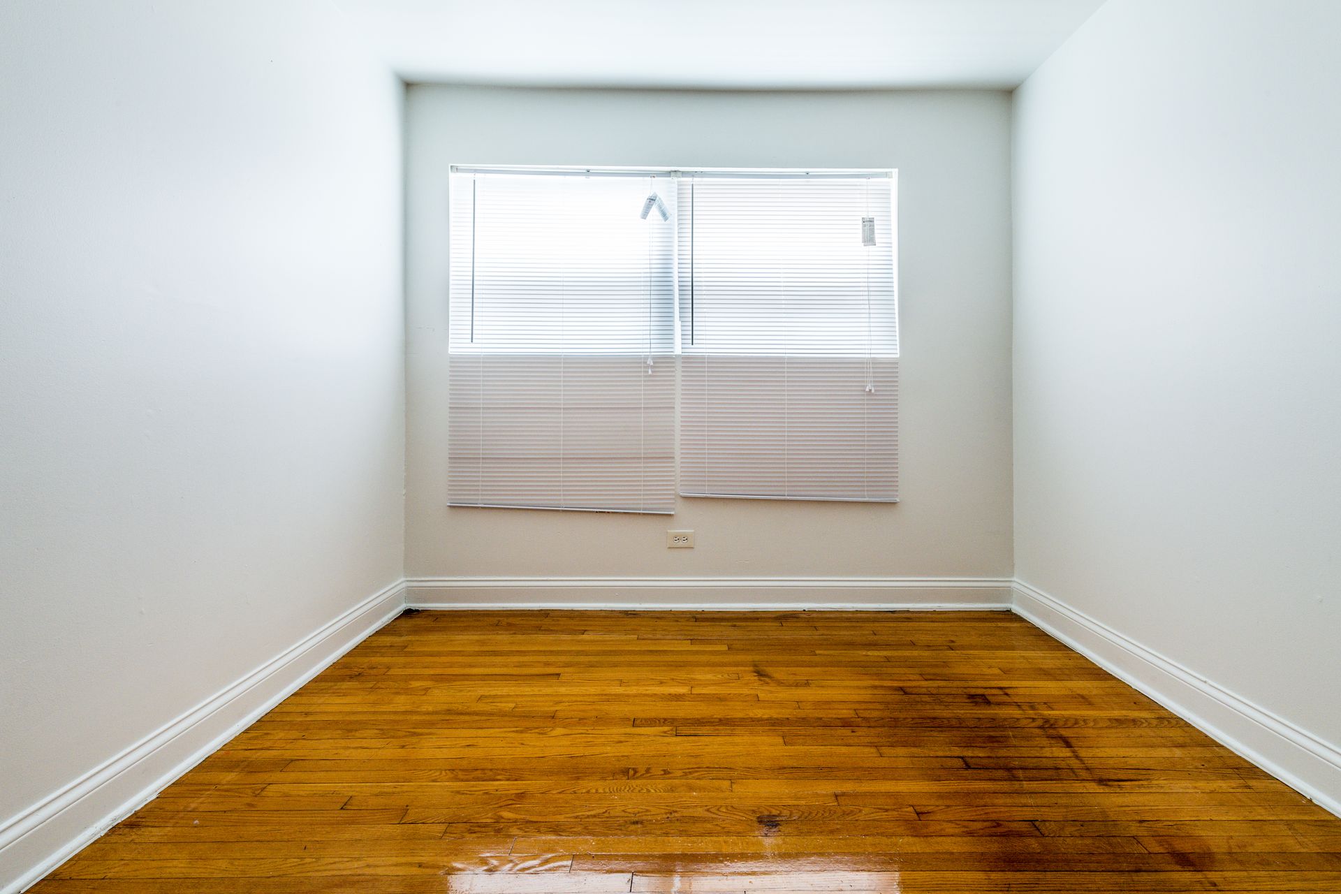 Empty room with hardwood floors, white walls, and a window with blinds.