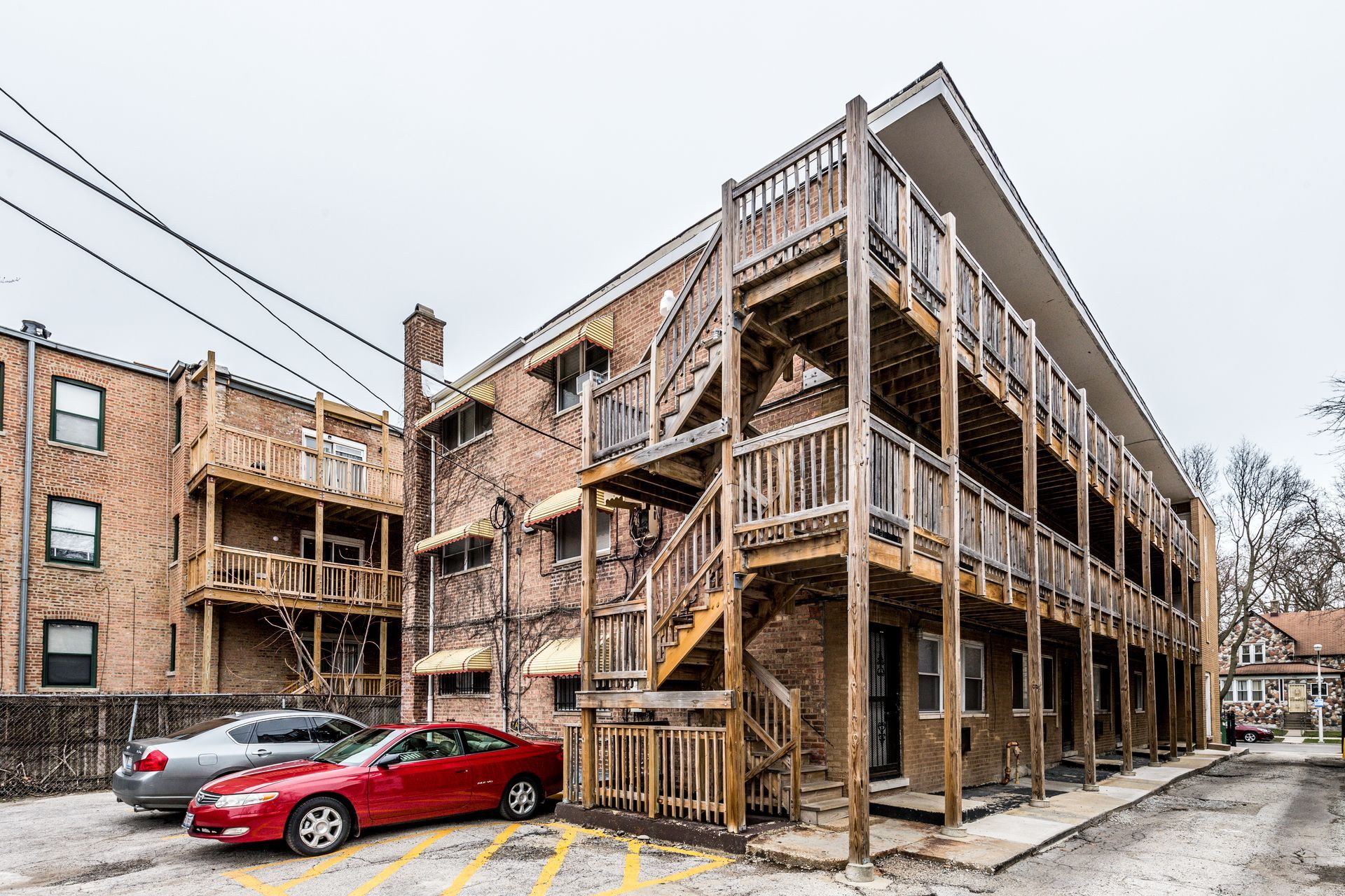 Apartment building with brick exterior, wooden balconies, and a red car parked out front.