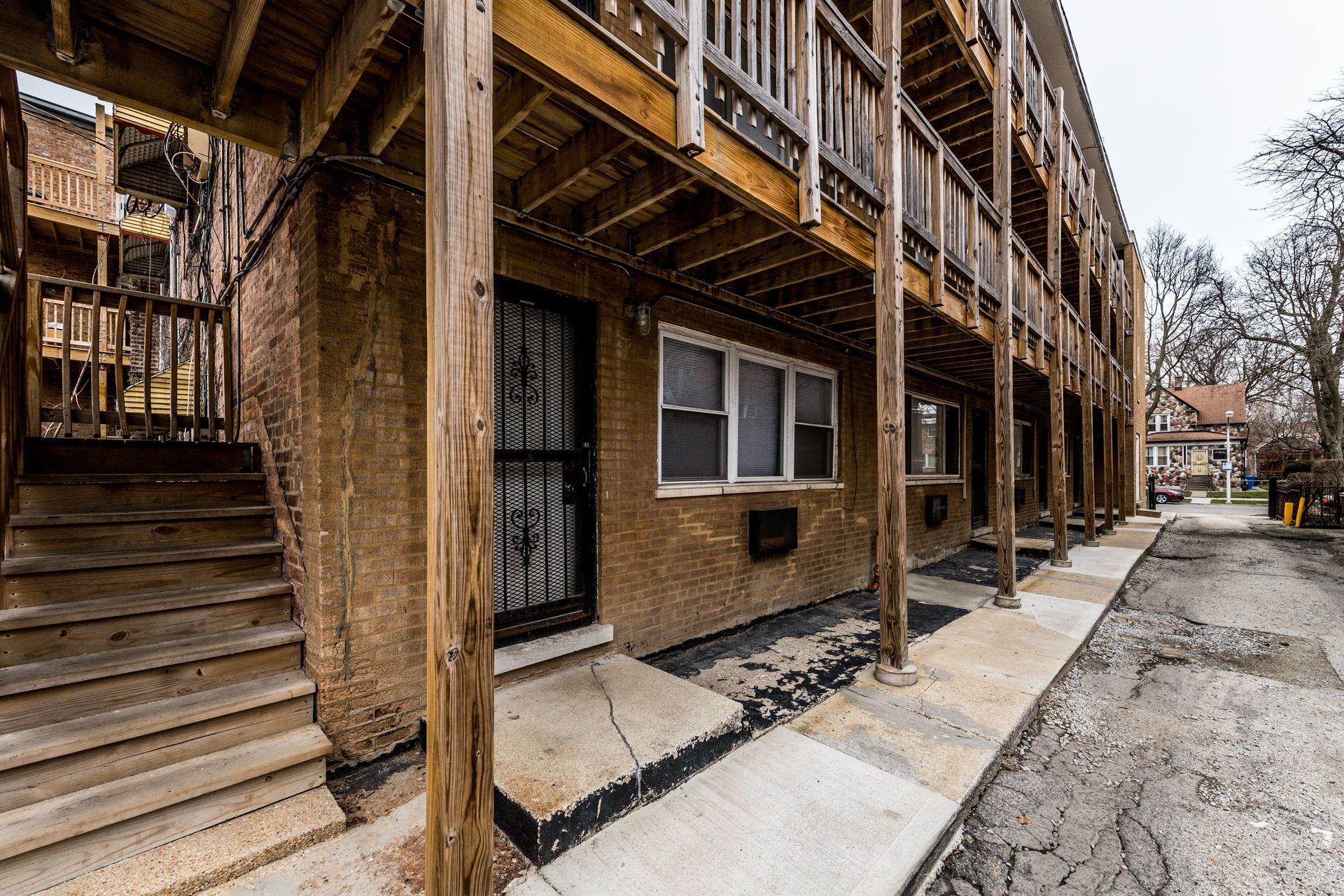 Exterior of a multi-unit building with wooden balconies, stairs, and a sidewalk.