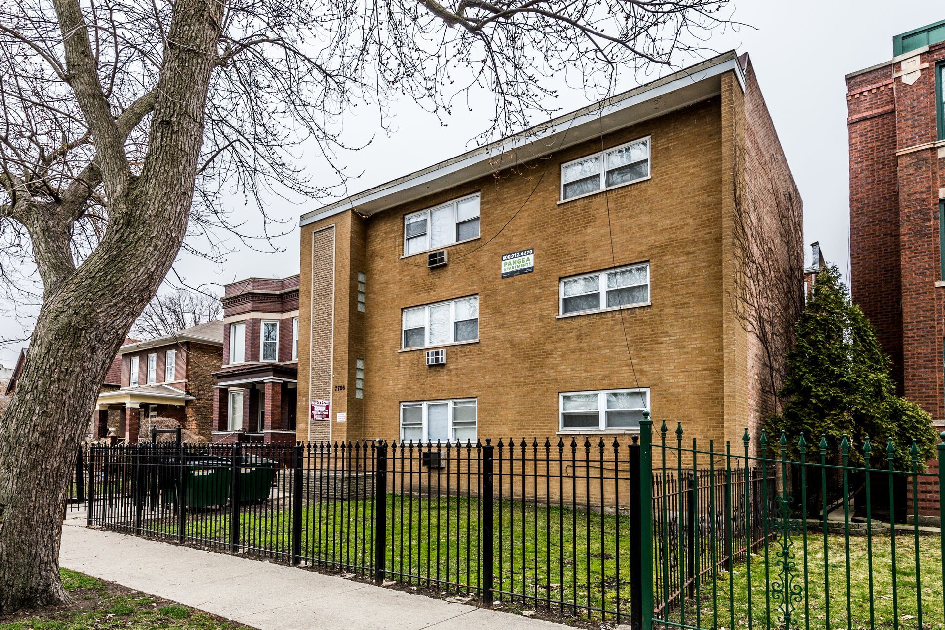Three-story brick building with multiple windows behind a black fence.