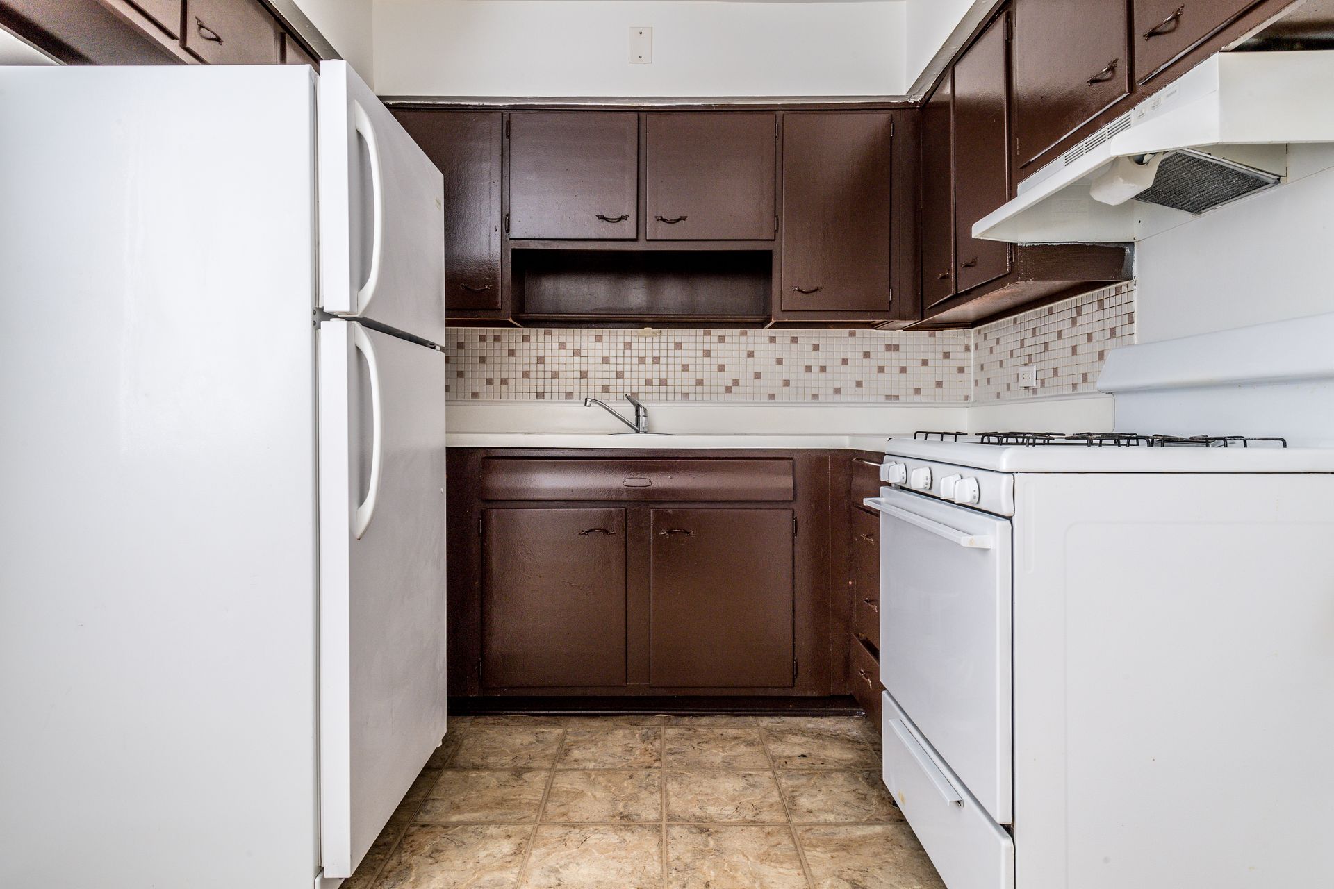 Kitchen with white appliances, brown cabinets, and patterned backsplash.