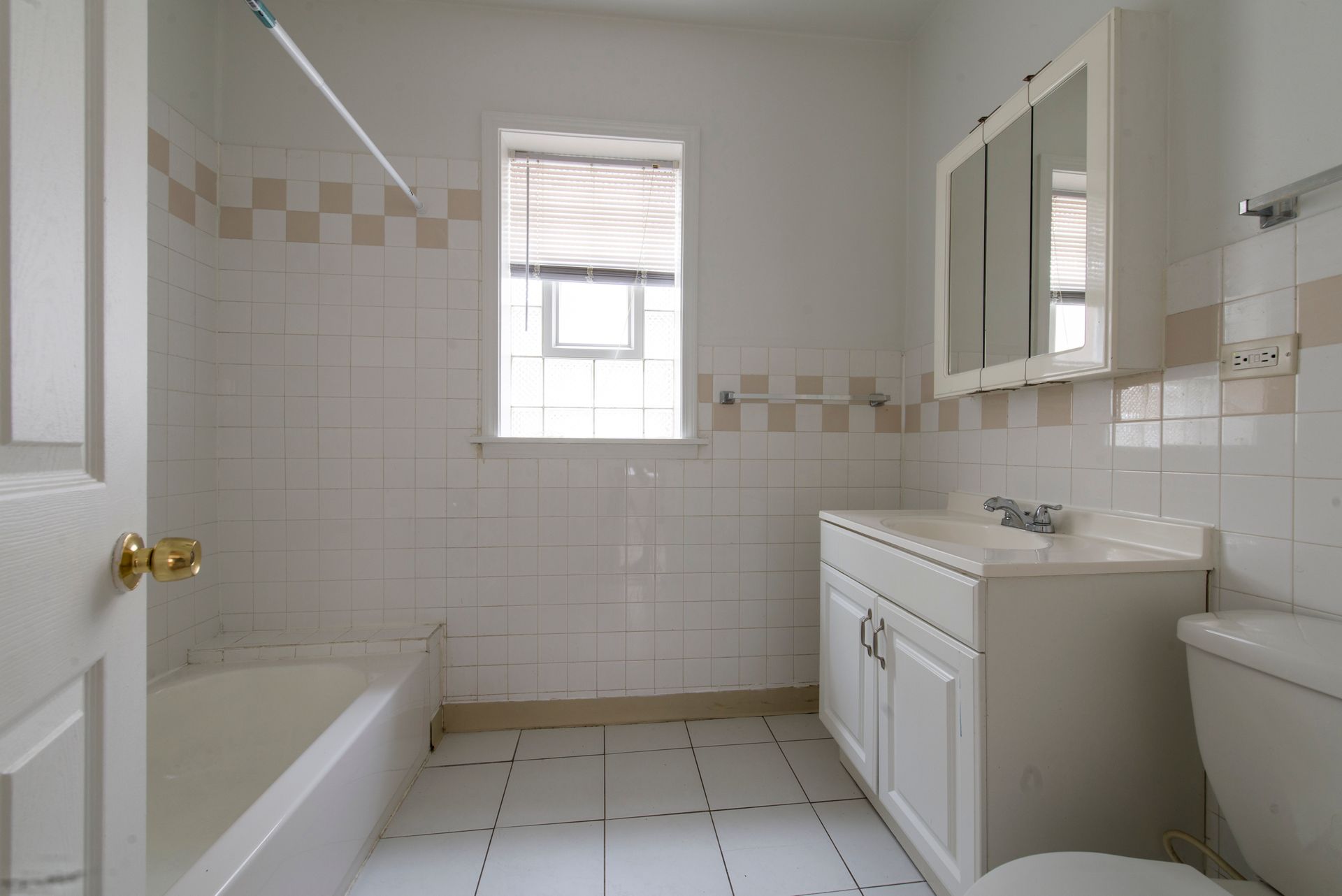 Bathroom with white tile walls, a bathtub, sink, toilet, and window.