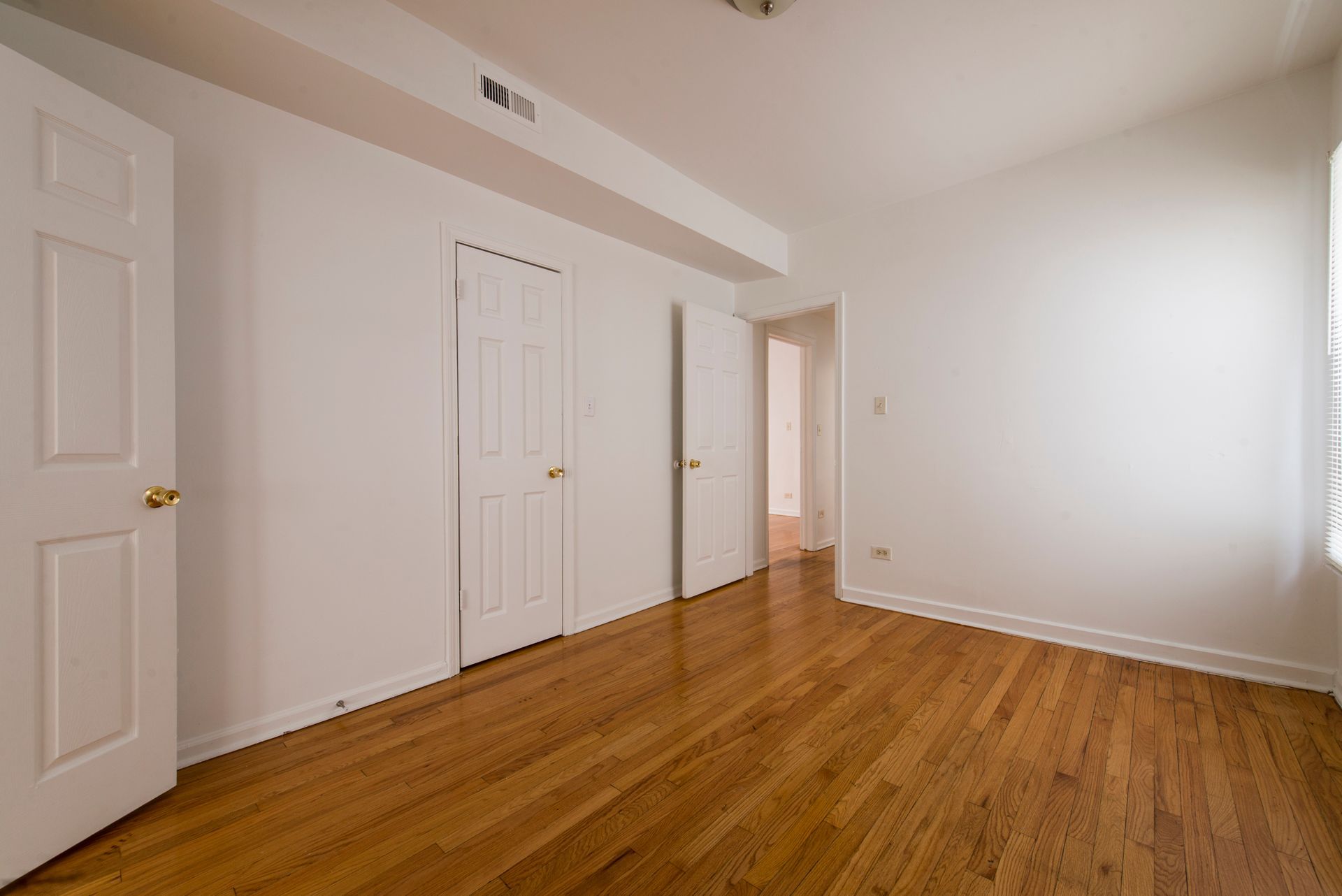 Empty room with hardwood floors, white walls, and three white doors.