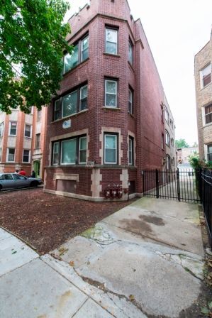 Brick apartment building with concrete parking area and gated entrance.