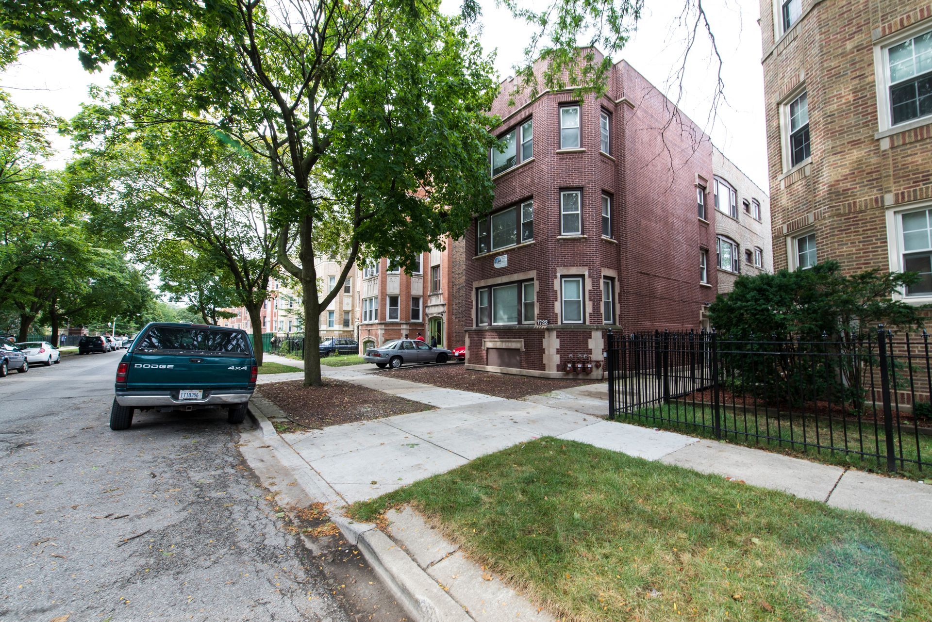 Green pickup truck parked on a residential street with apartment buildings. Trees and sidewalk are in view.