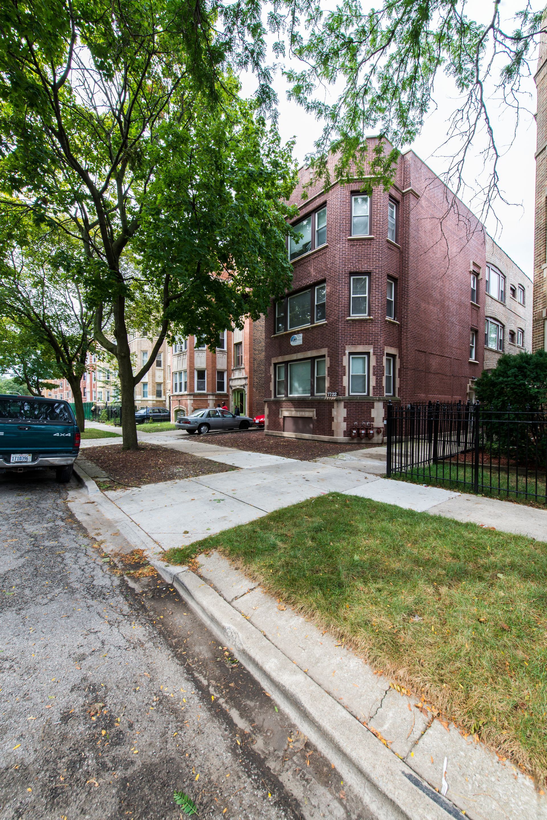 Brick apartment building on a residential street; tree and green lawn in foreground.