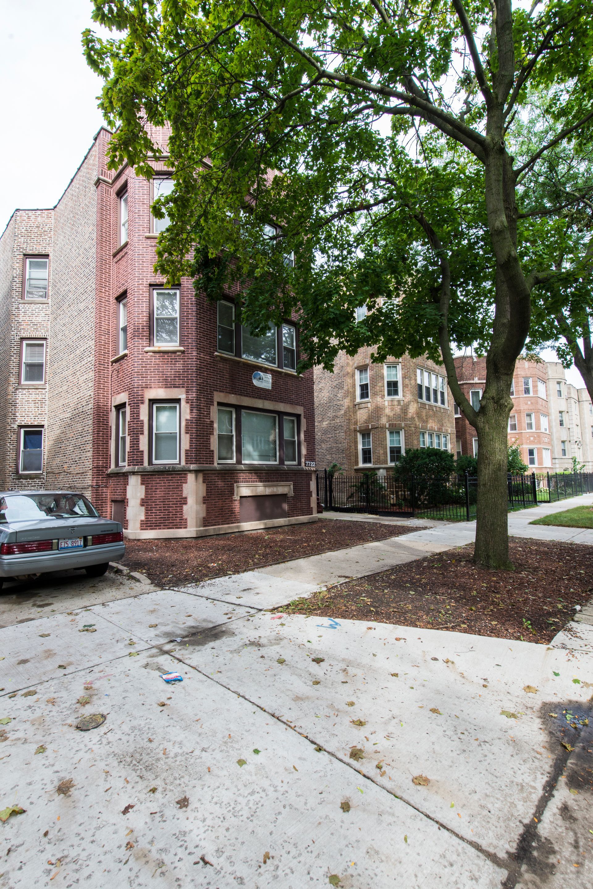 Brick apartment buildings on a city street, one with a bay window, a parked car, and a tree.