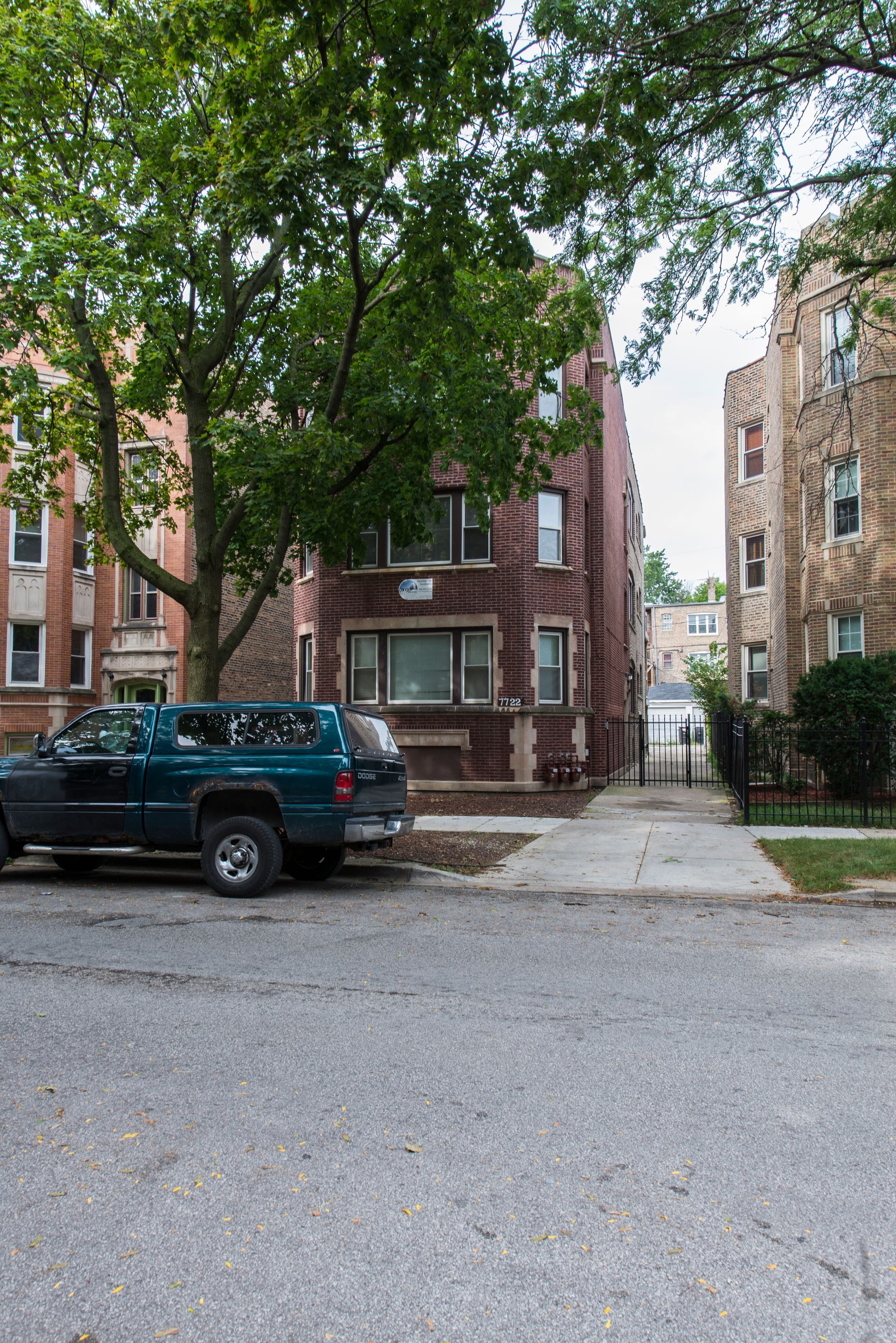Street view of brick apartment buildings, a parked truck, and a tree.