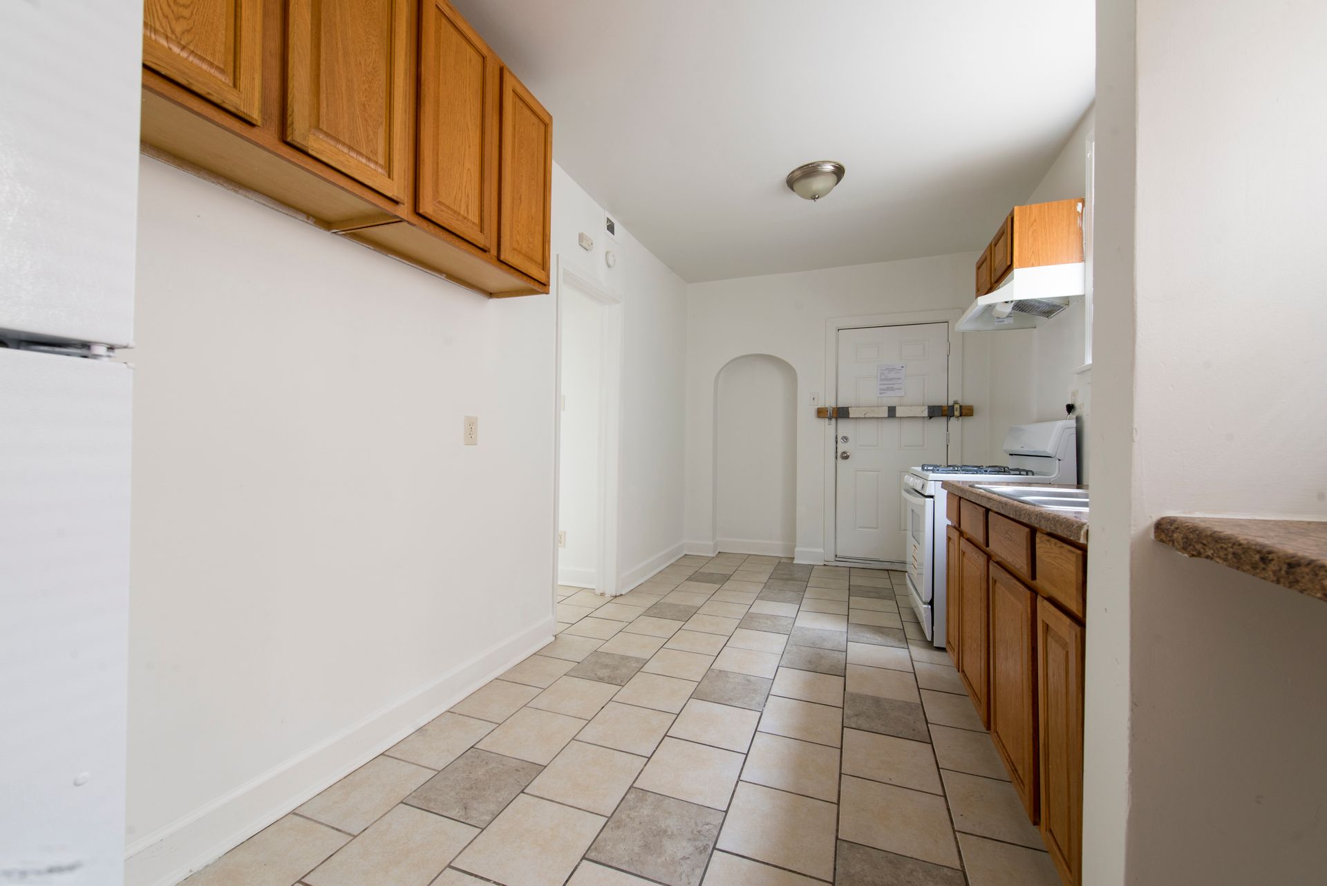 Empty kitchen with light-brown cabinets, white walls, and checkered tile floor.