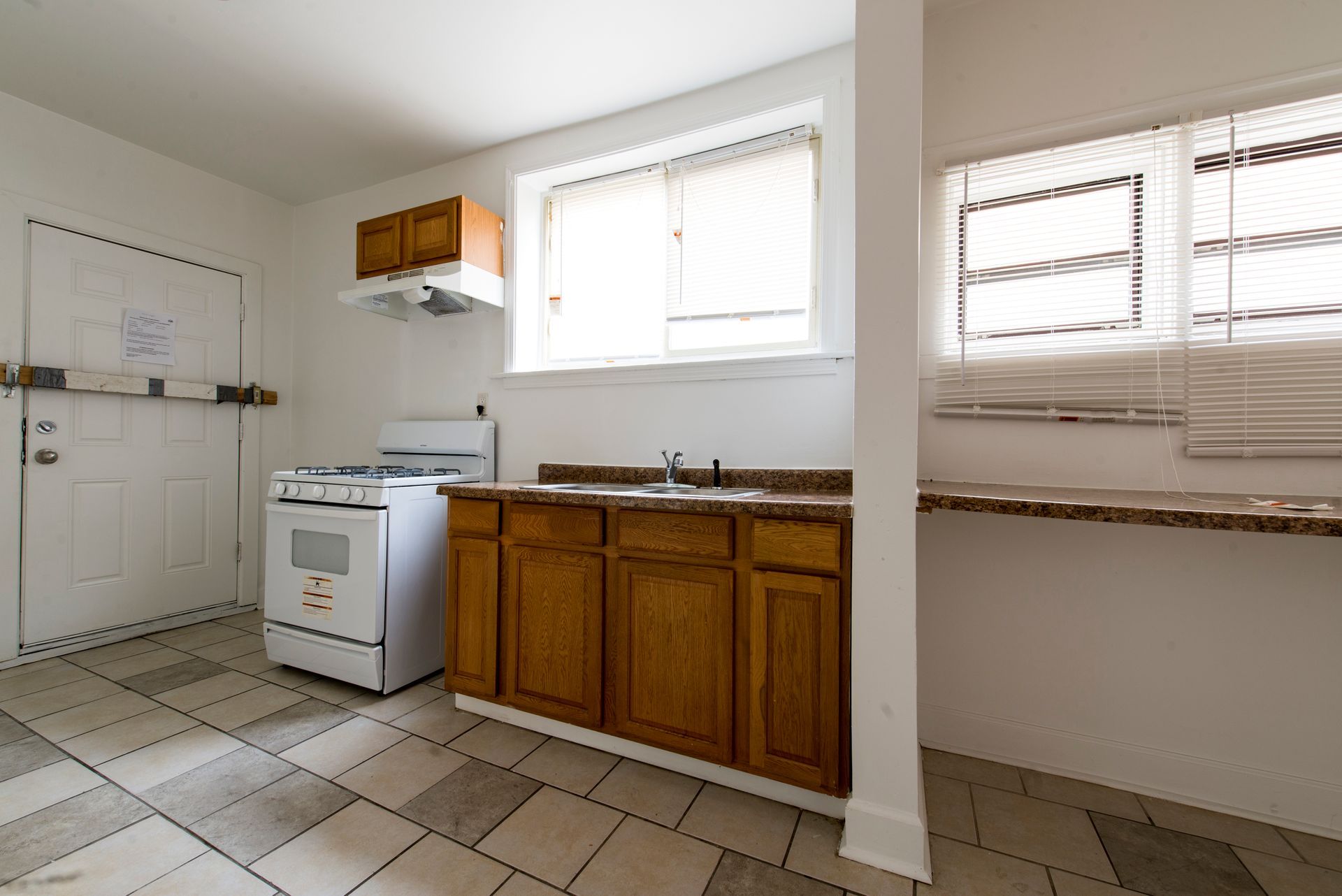 Kitchen with cabinets, stove, sink, window, and white door. Tile floor and neutral colors.