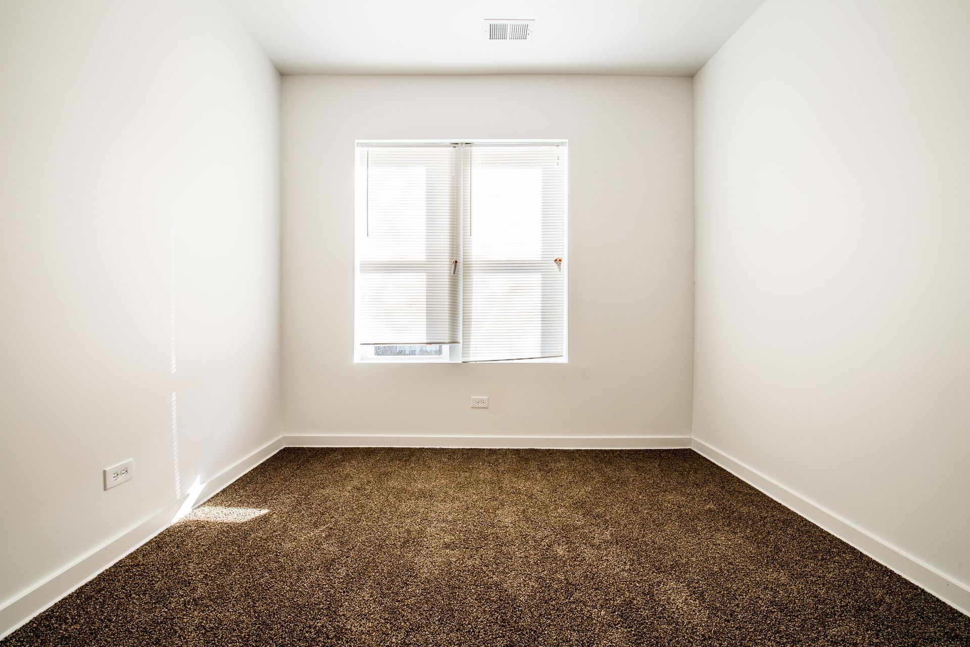 Empty room with brown carpet, white walls, and a window with blinds.