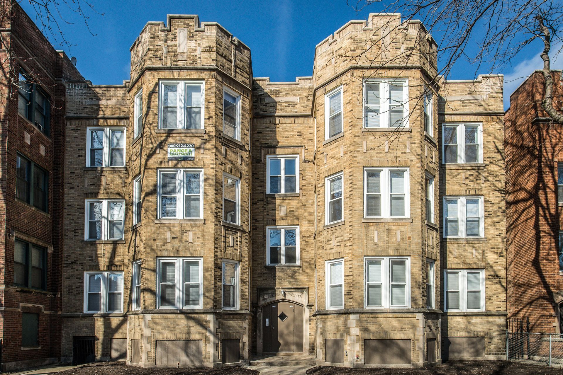 Tan brick apartment building with white-framed windows, against a blue sky.