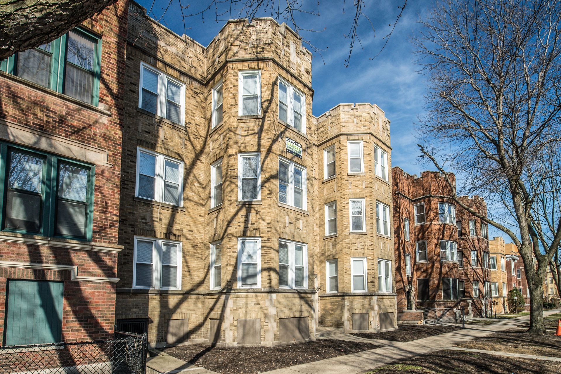 Brick apartment buildings with arched bay windows and shadows cast by bare trees.