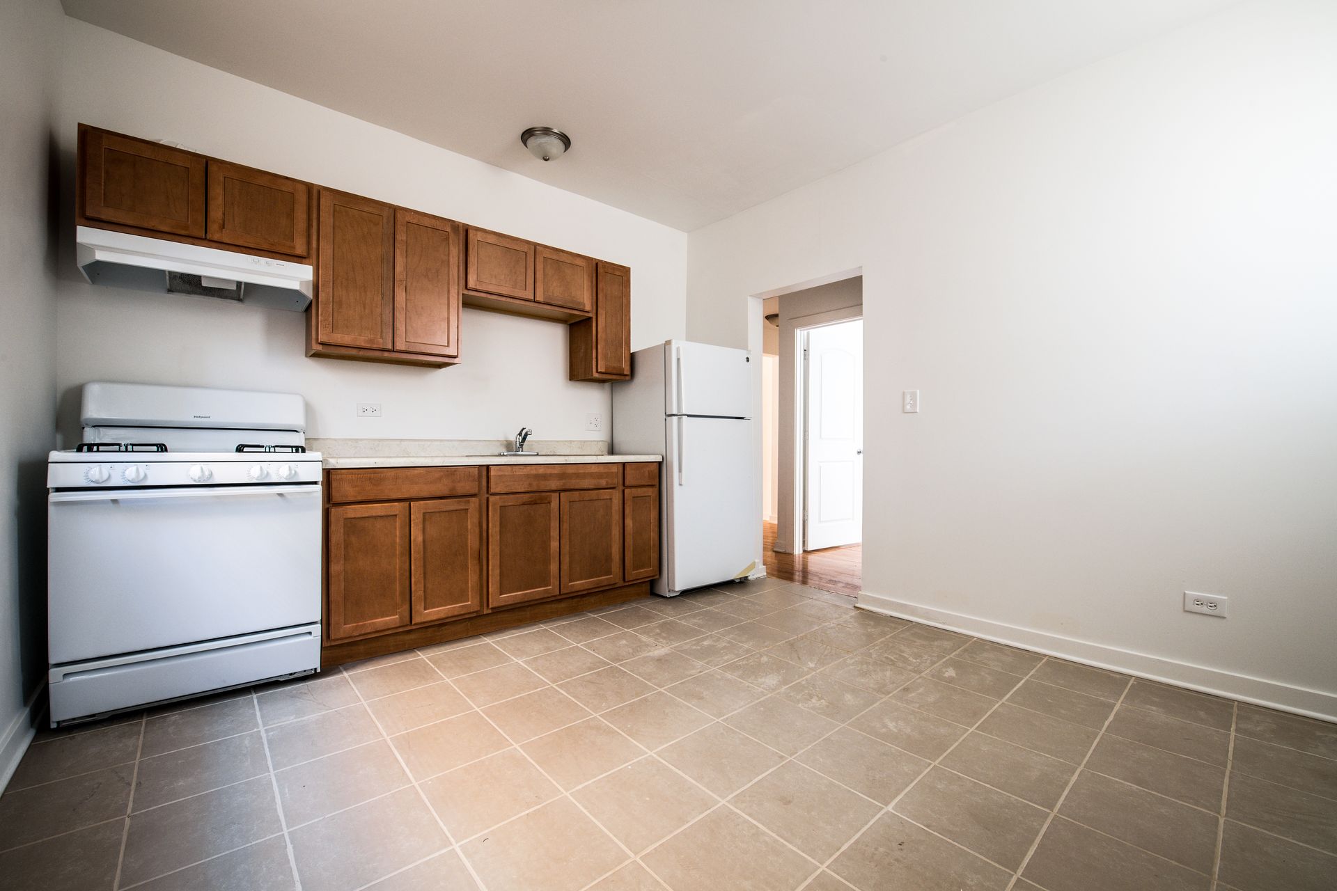 Small kitchen with brown cabinets, white appliances, and tan tile floor.