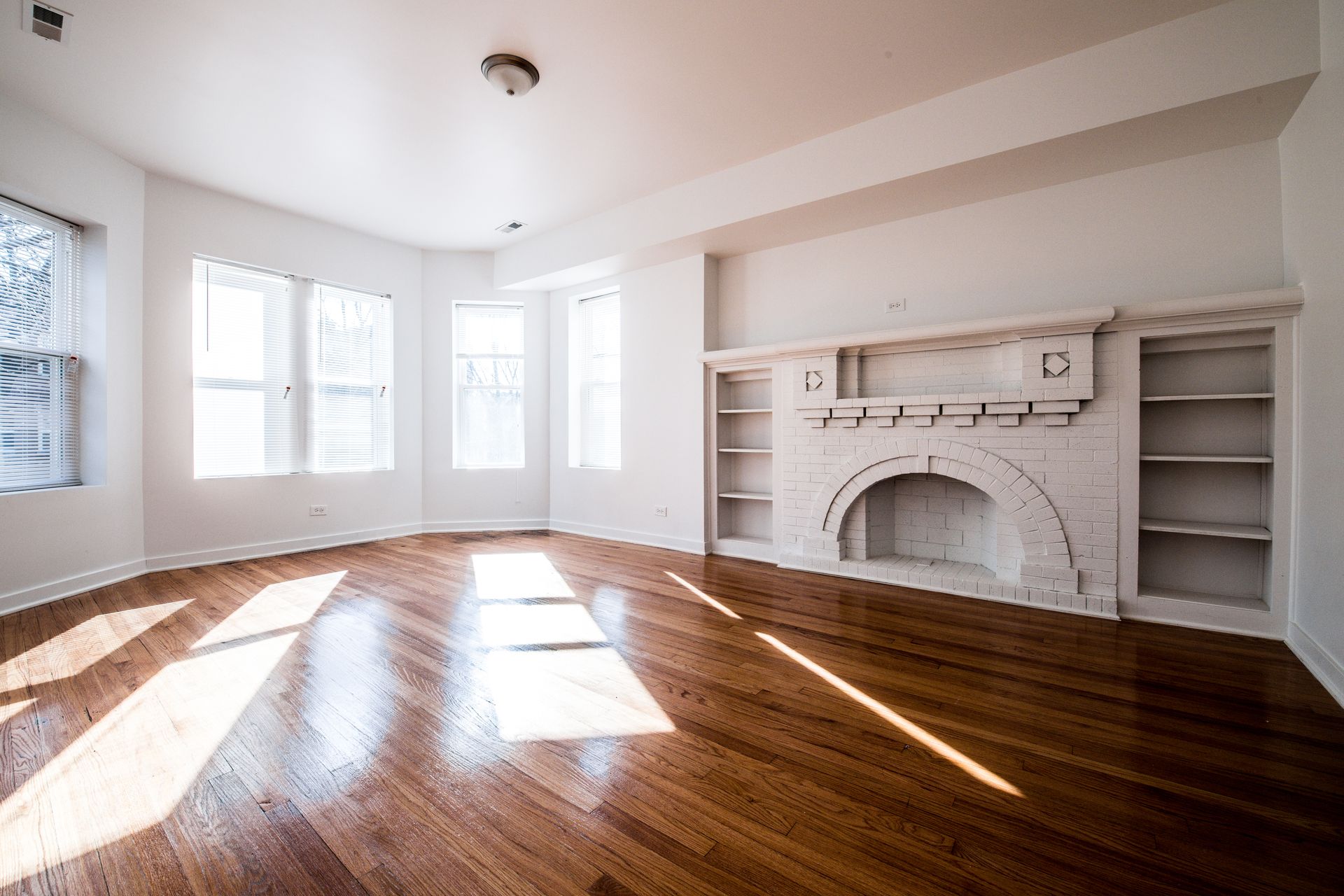 Empty room with hardwood floors, white walls, and a fireplace with built-in shelves.