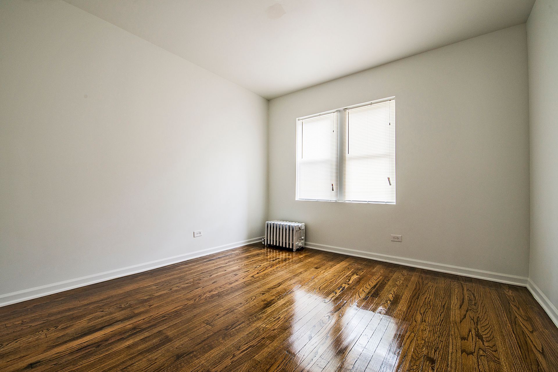 Empty room with wood flooring, white walls, and a window with blinds.