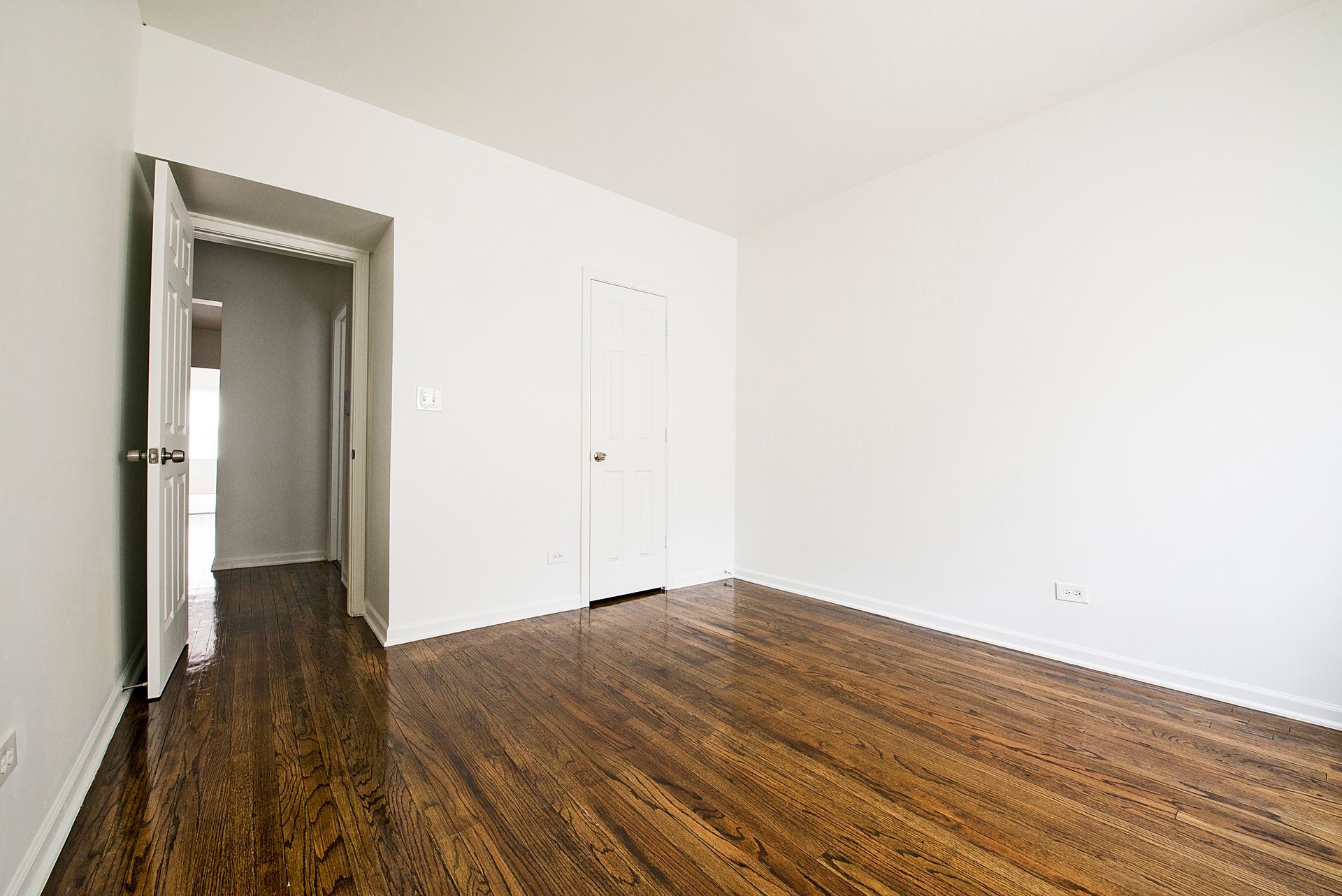 Empty room with hardwood floors, white walls, and a doorway.
