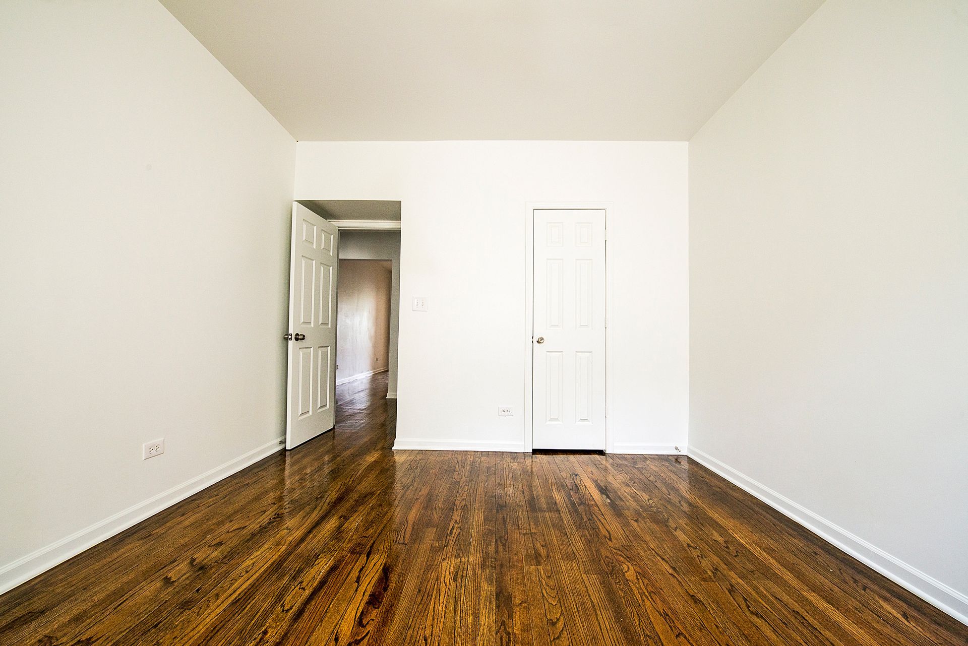 Empty room with hardwood floors, white walls, and an open doorway leading to a hallway.