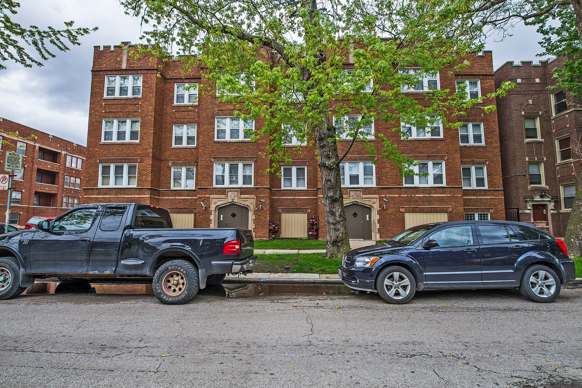 Brick apartment building with dark cars parked in front.