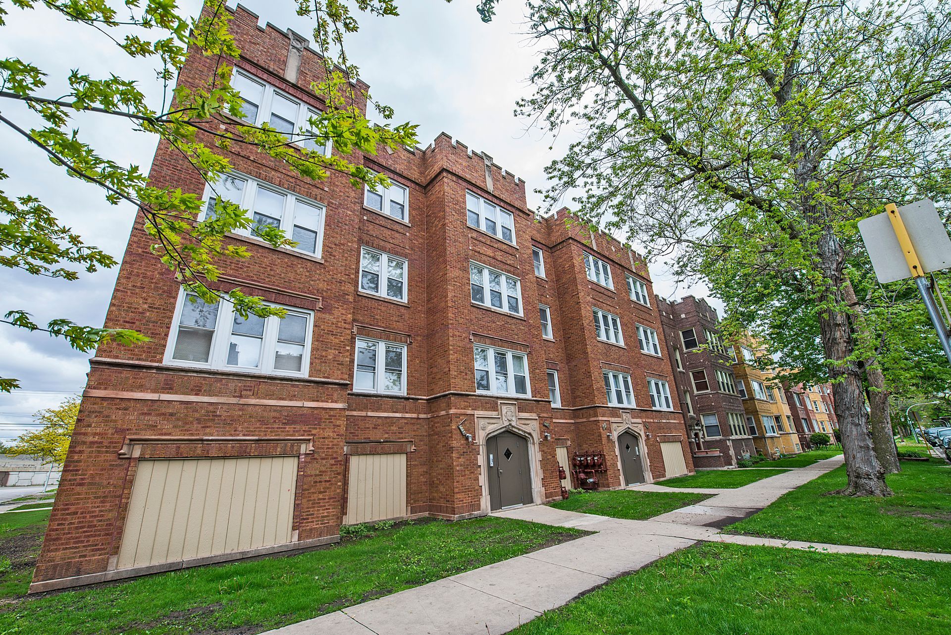 Brick apartment building with arched windows, lawn, and sidewalk.