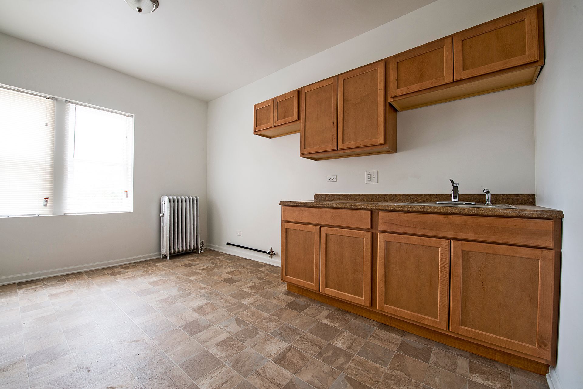 Empty kitchen with brown cabinets and countertop, window, and radiator.