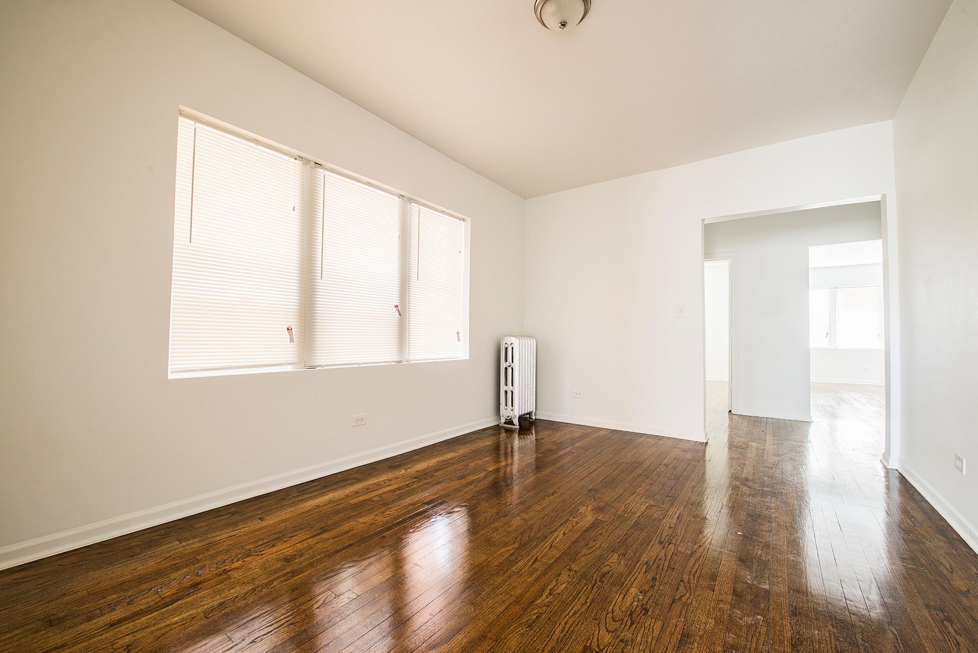 Empty room with hardwood floors, a window with blinds, and a doorway.