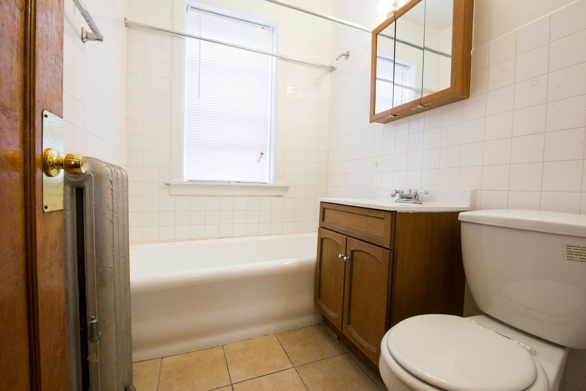 Bathroom with white tile walls, a bathtub, wooden vanity, and toilet.