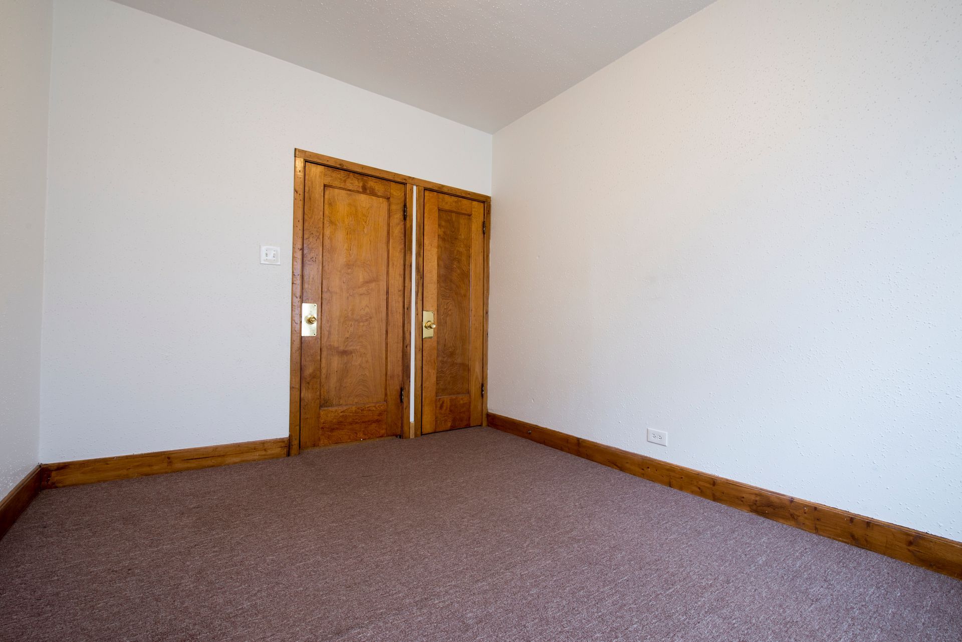 Empty room with brown carpet, wooden trim, and closet doors.