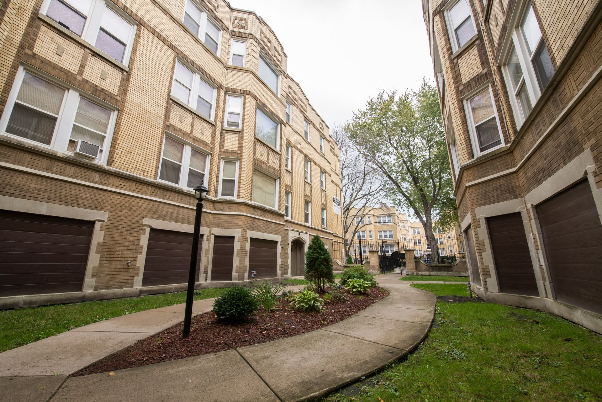Apartment complex exterior with brick buildings, garages, and a curved walkway.