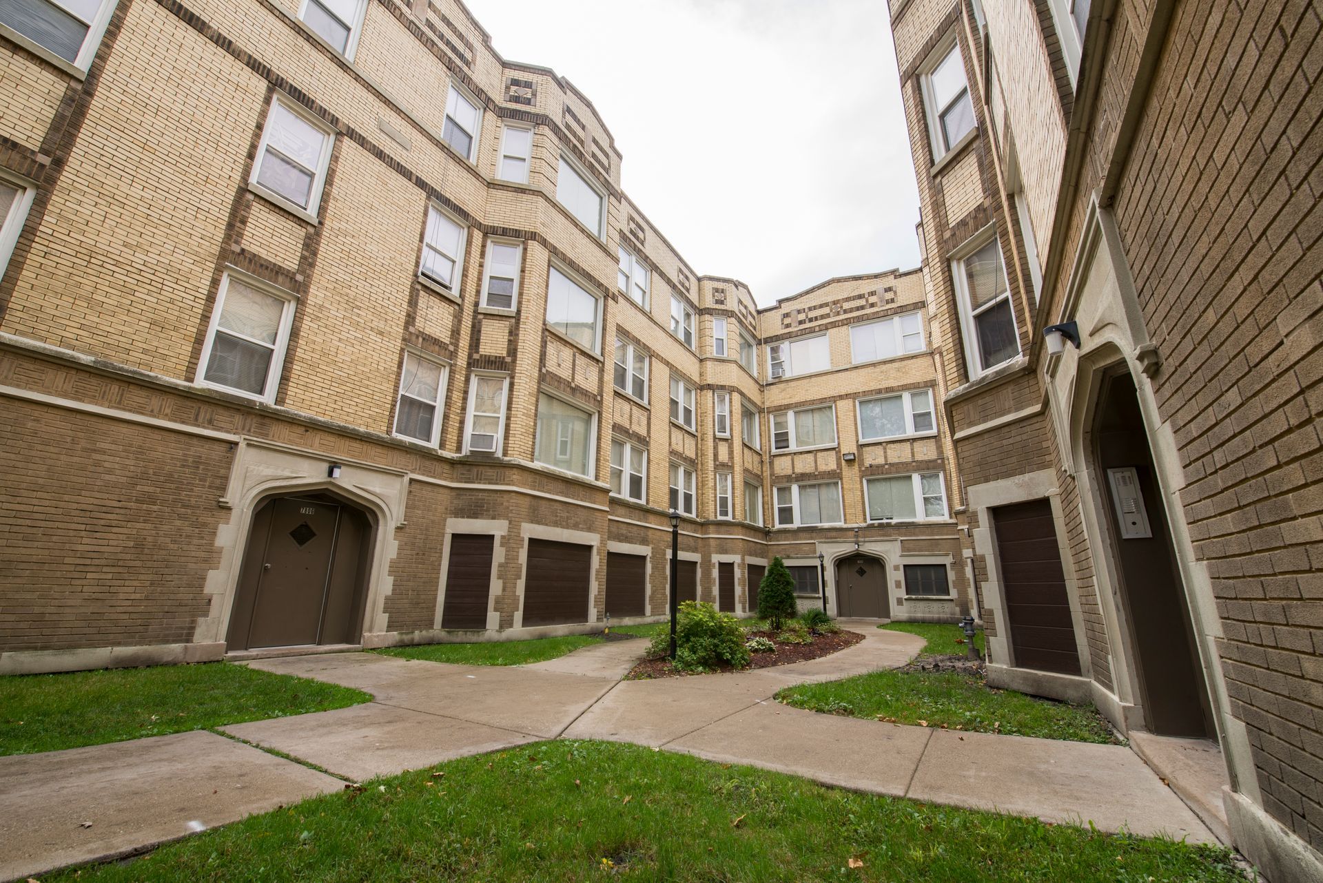 Courtyard of a multi-story brick apartment building with brown doors and green grass.