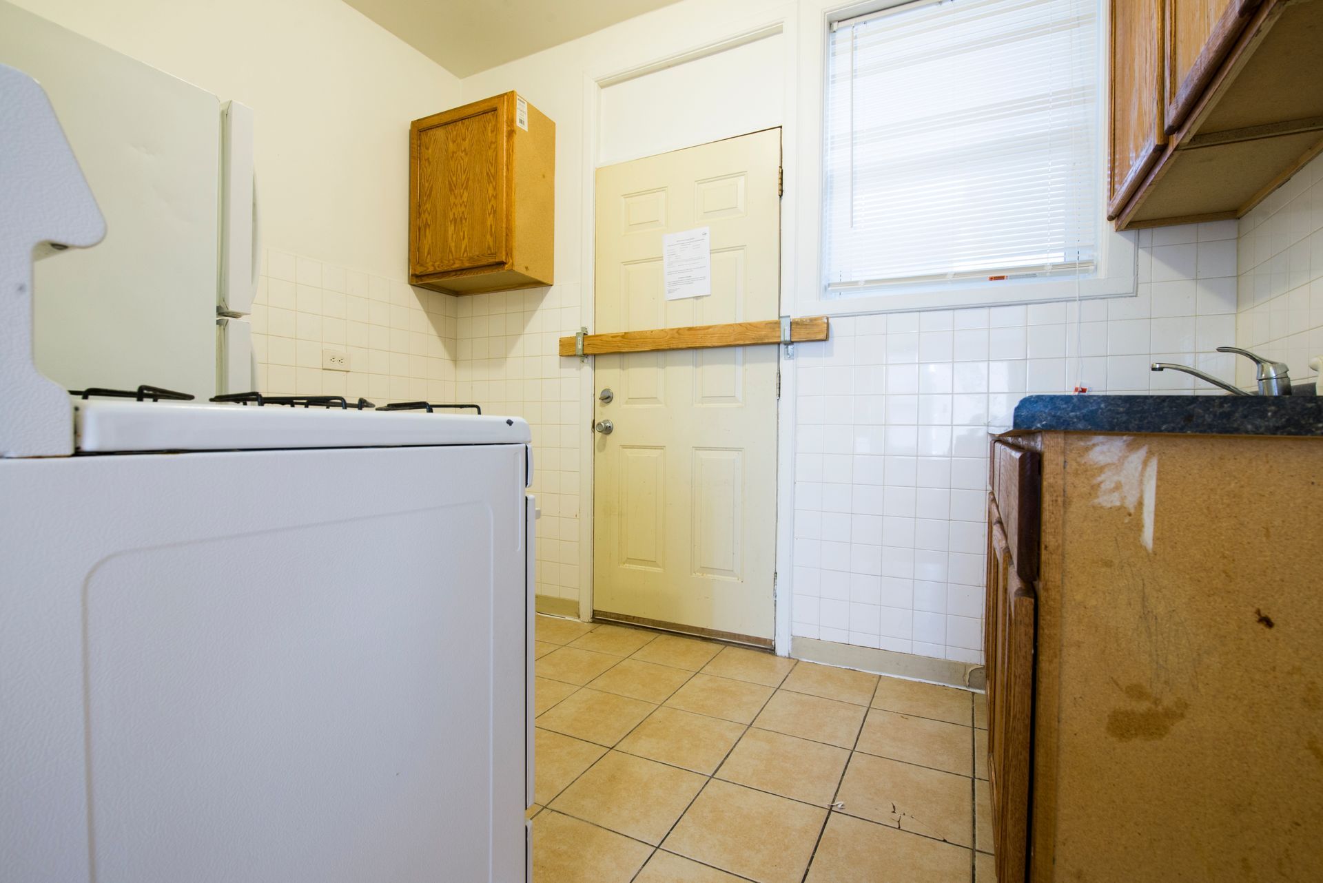 White stove in a small kitchen with worn cabinets, door, and tiled backsplash.