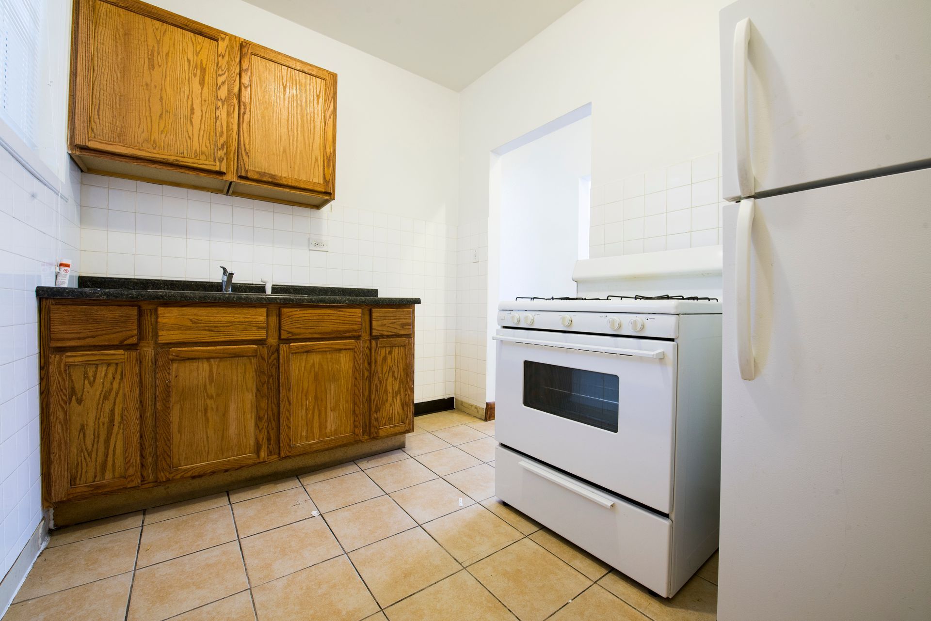 Kitchen with wood cabinets, white appliances, tile floor, and open doorway.