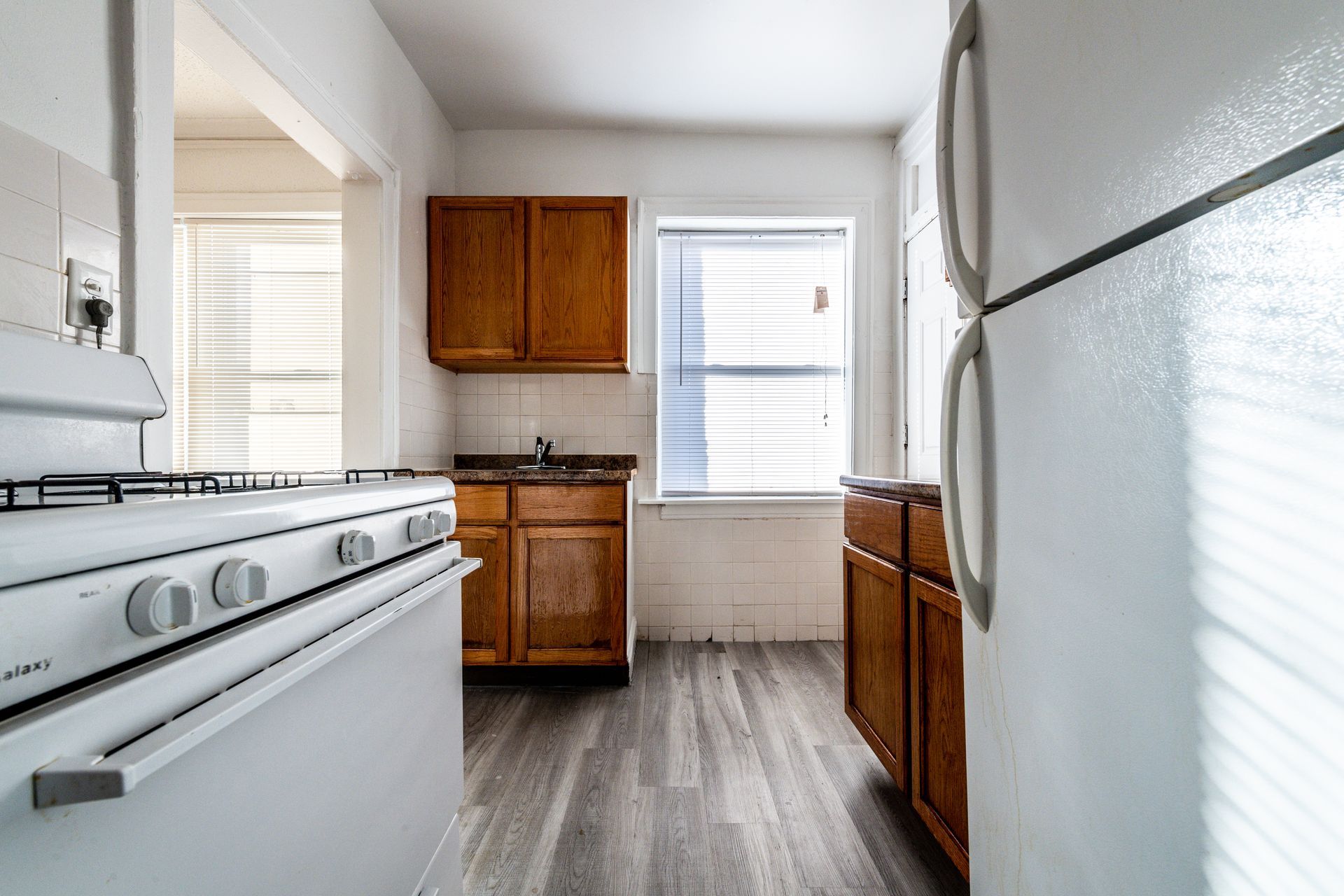 Kitchen with white appliances, brown cabinets, and a window with blinds.
