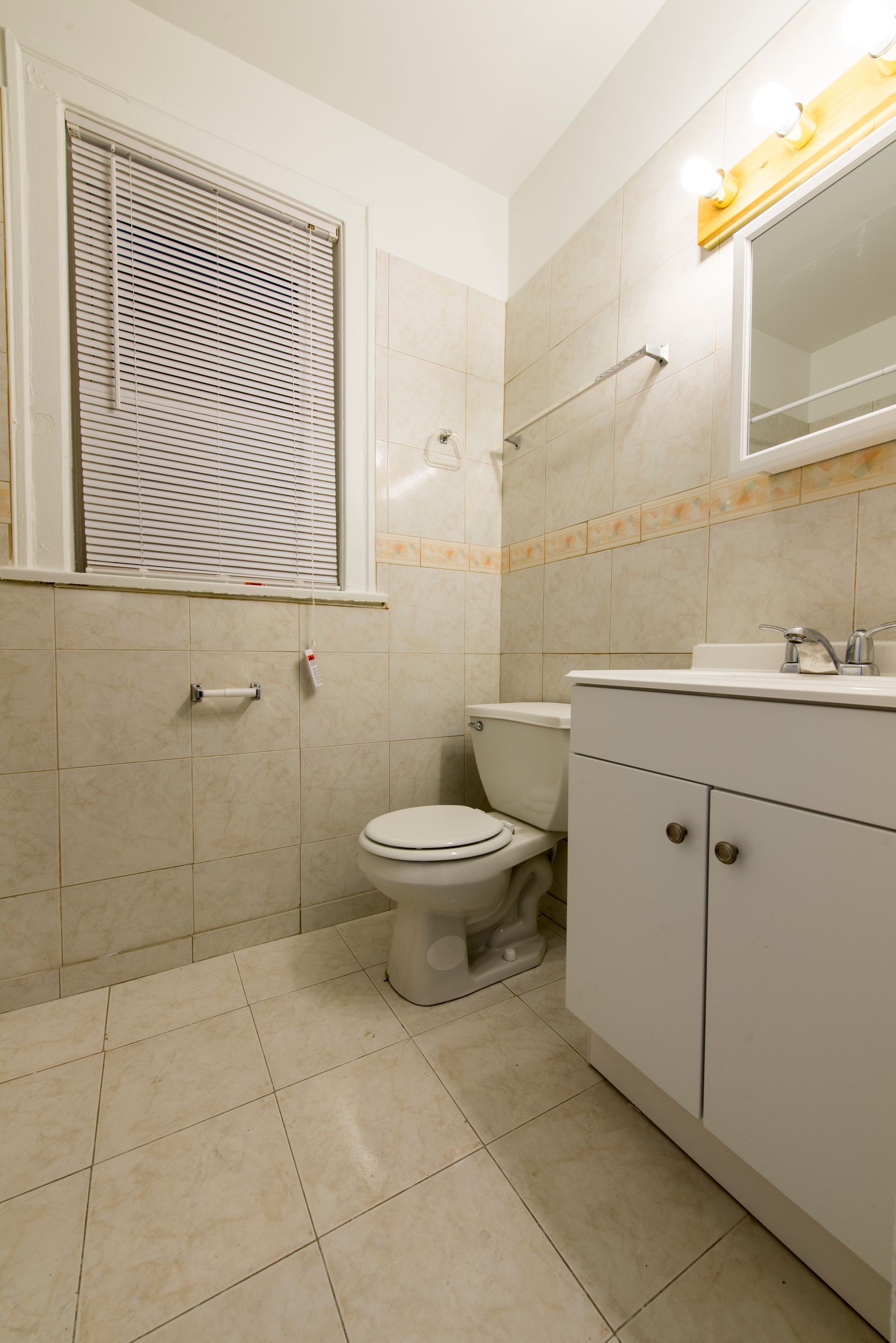 Bathroom with a toilet, vanity, and window with a geometric pattern, neutral tones.