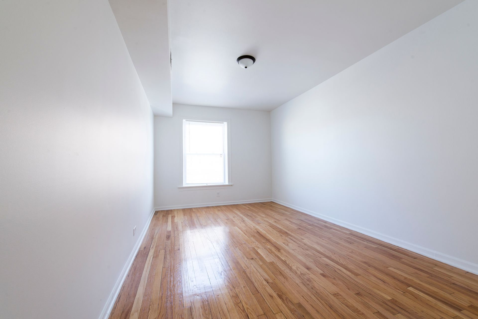 Empty room with hardwood floors, white walls, and a window.