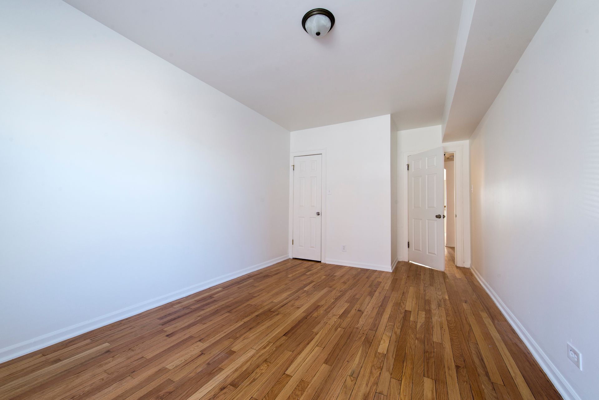 Empty room with hardwood floors, white walls, two closed doors, and a light fixture.