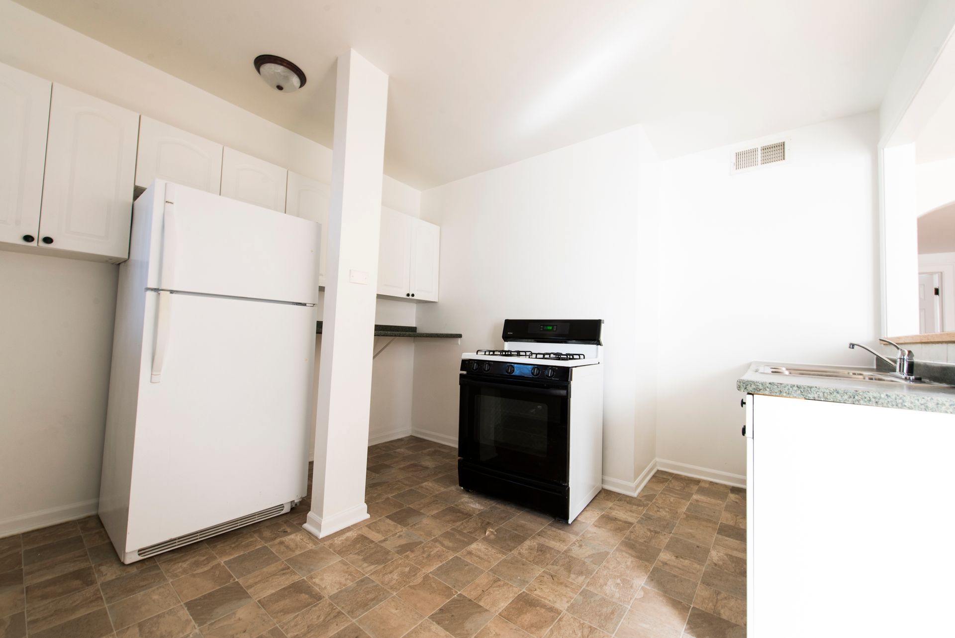 White kitchen with a refrigerator, cabinets, stove, and column.