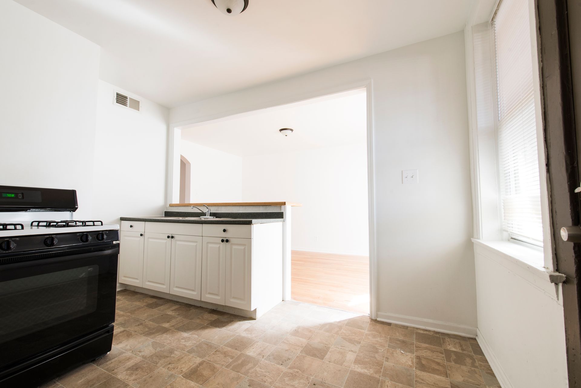 Empty kitchen with white cabinets, black stove, and doorway to living area.