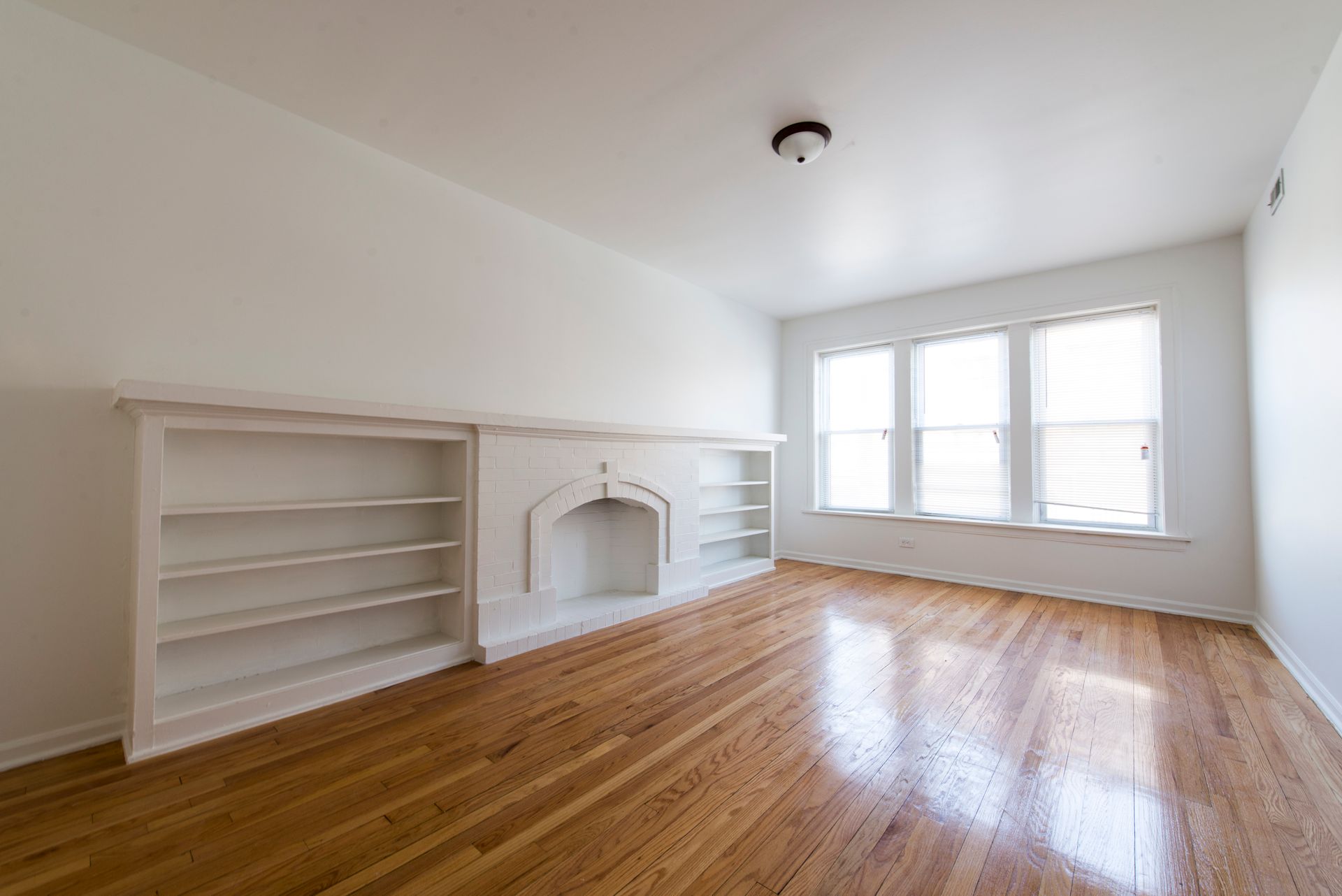 Empty room with hardwood floors, built-in bookshelves and fireplace, and three windows.